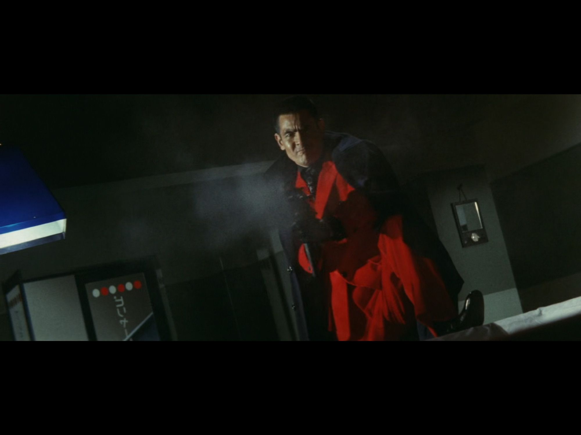 Bunta in an outrageously swagged out red suit, one leg up on a table, machine gun dragoning someone