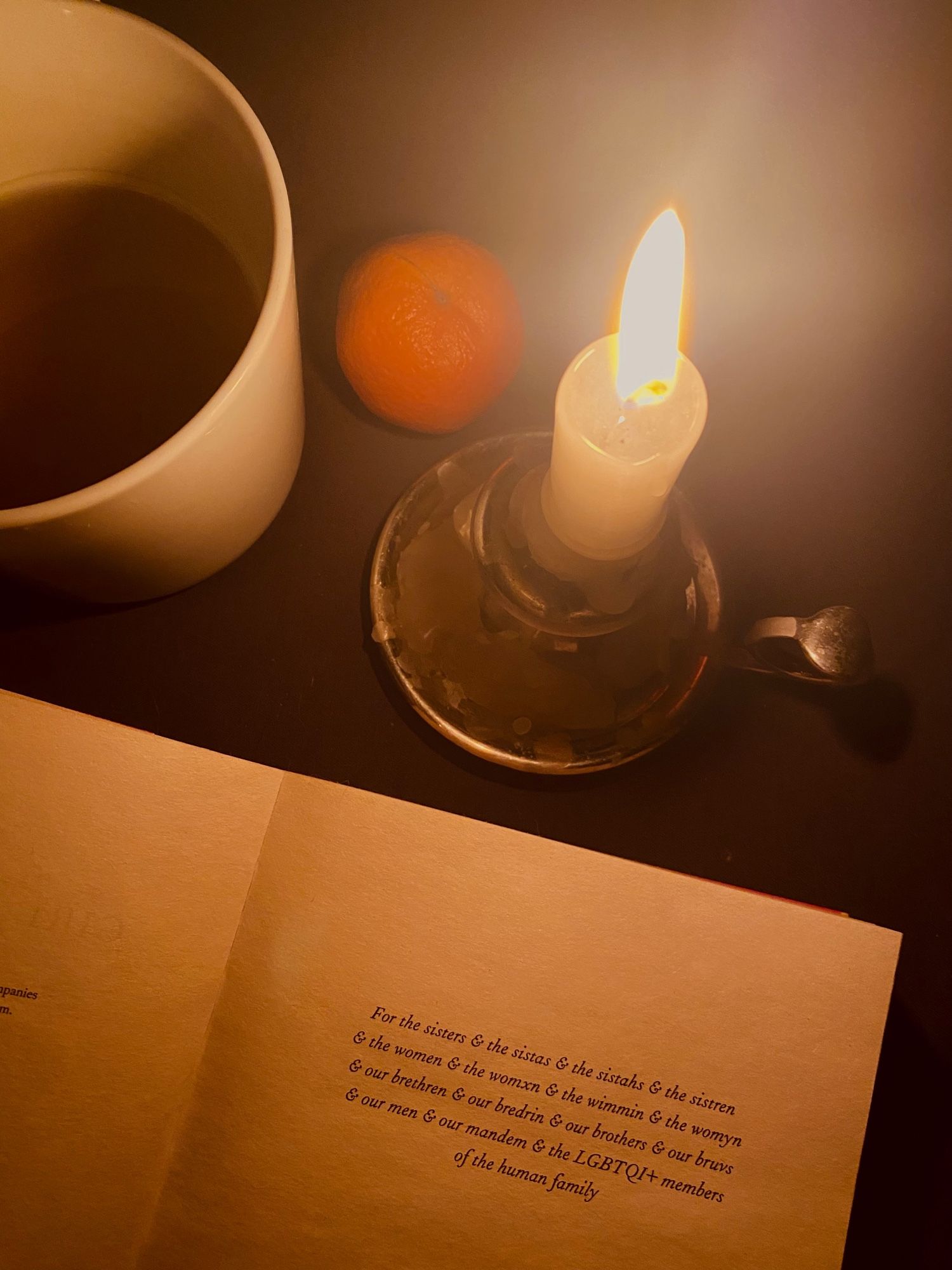 An open book, a candle, a tangerine and a mug with tea.