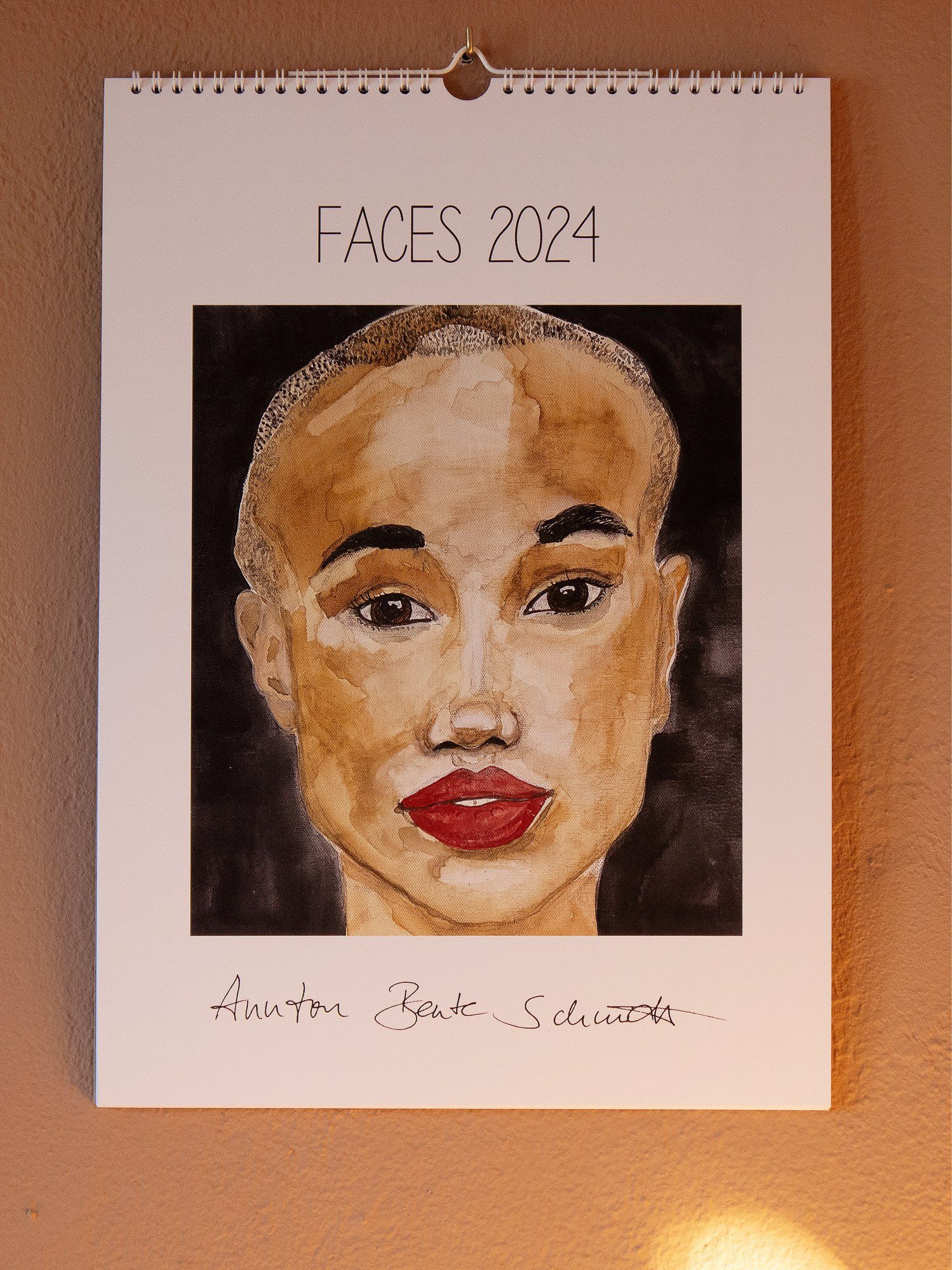 Cover page of FACES 2024 hanging on a wall, showing the portrait of a black woman with very short hair and bright red lips.