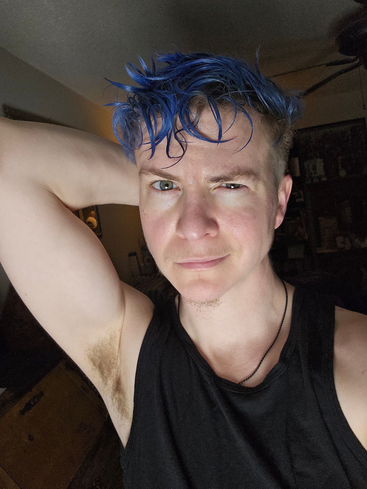 White genderqueer person with messy curly cobalt blue hair and stormy blue eyes wearing a black tanktop, holding one casually muscular arm flexed behind their head and smirking fiercely, with one eyebrow quirked suggestively