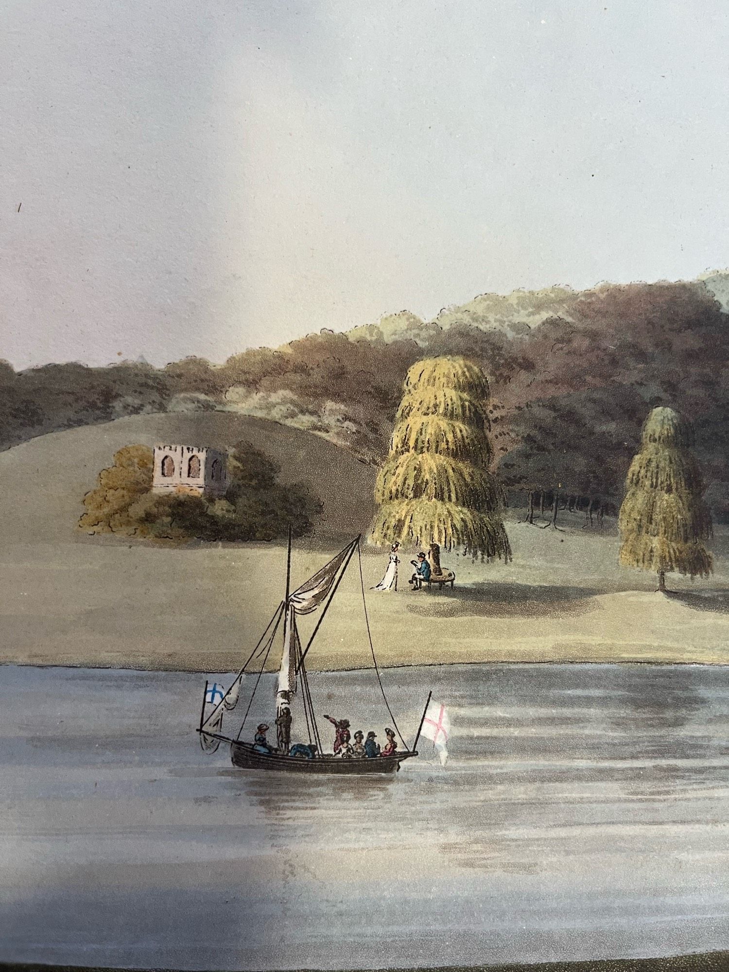 Coloured view of an elite designed landscape with a lake in the foreground on which there is a small boat with several passengers- presumably having fun on the water