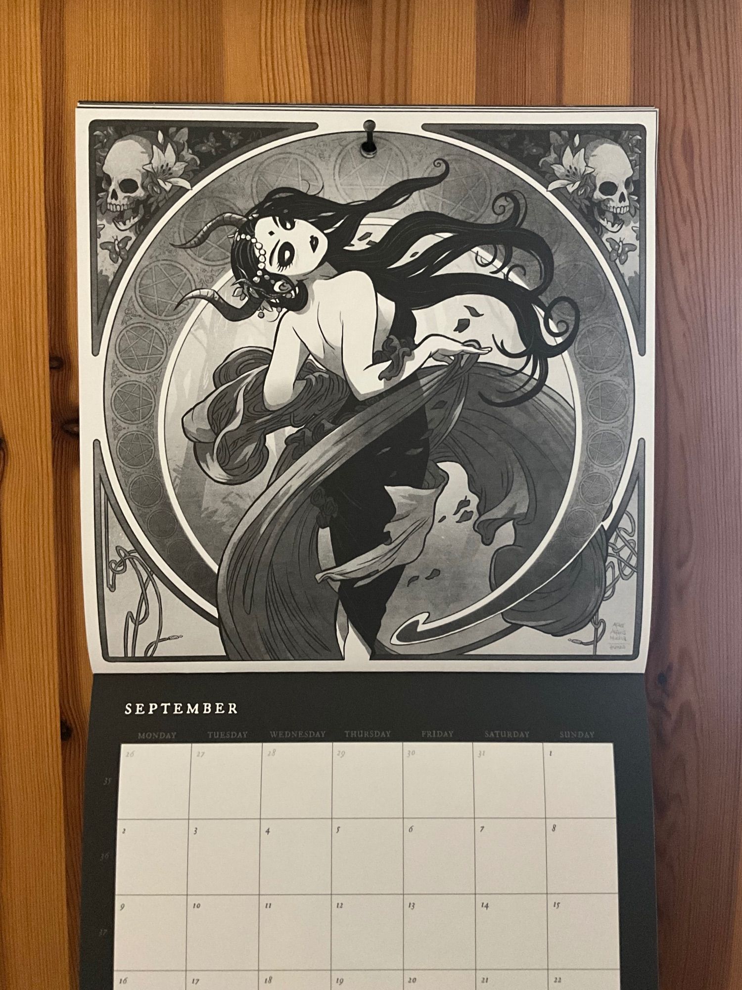 Photo of the September 2024 Belzebubs wall calendar picture, an homage for The Arts: Dance by Alphonse Mucha, done in Belzebubs style. Black and white, horns, corpse paint, skulls, the works.