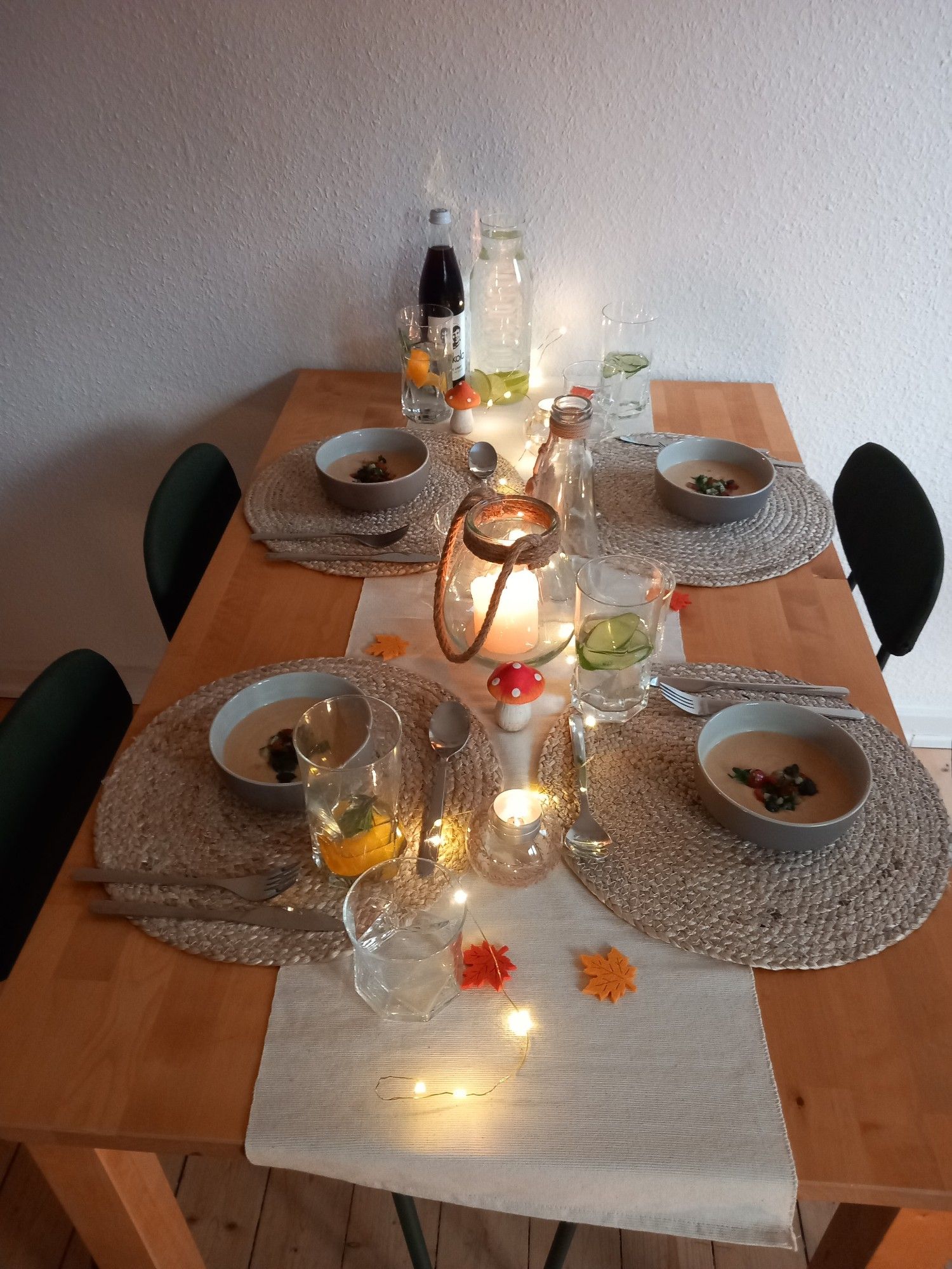 Herbstlich dekorierter Esstisch, eingedeckt für 4 Personen. Auf runden, Sisal- Platzdeckchen ist der erste Gang- eine Blumenkohl-Kokossuppe mit Salsa- bereit gestellt. Teelichter und eine dezente Lichterkette in der Tischmitte.