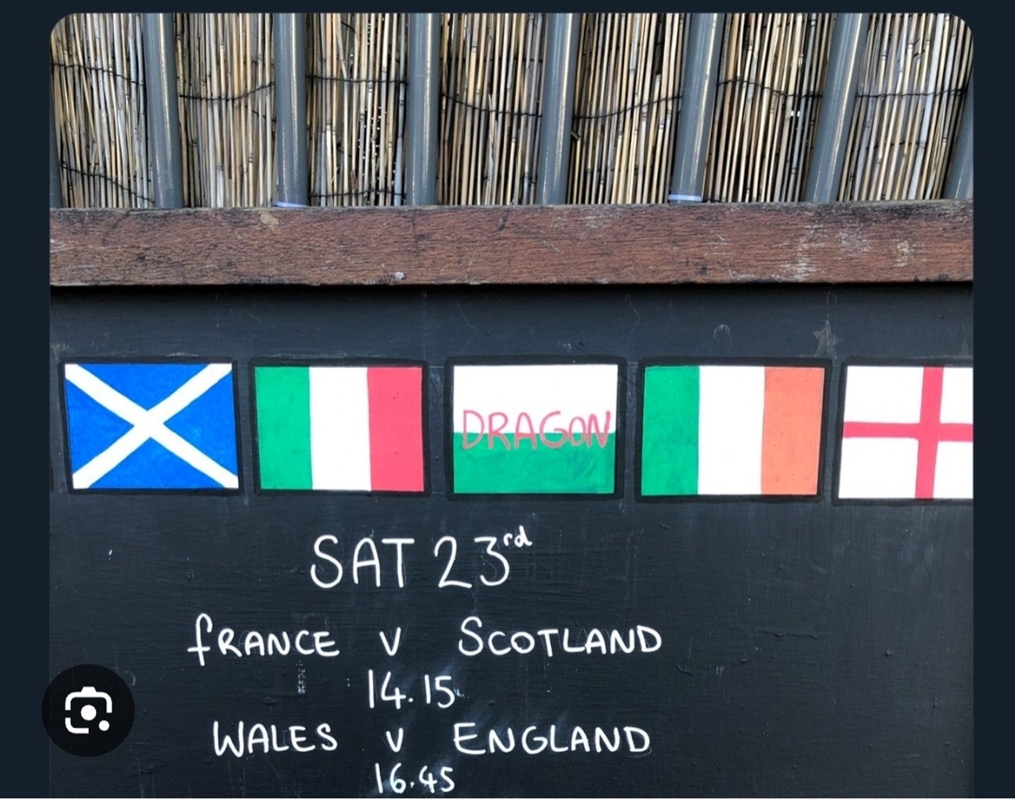 Photo from outside the Druid's Pub in Brighton. Chalkboard with the men's Six Nations matches of the day written on it, accompanied by drawings of the six national flags. The Welsh flag is a green ground and white sky, with the word 'DRAGON' written in red.