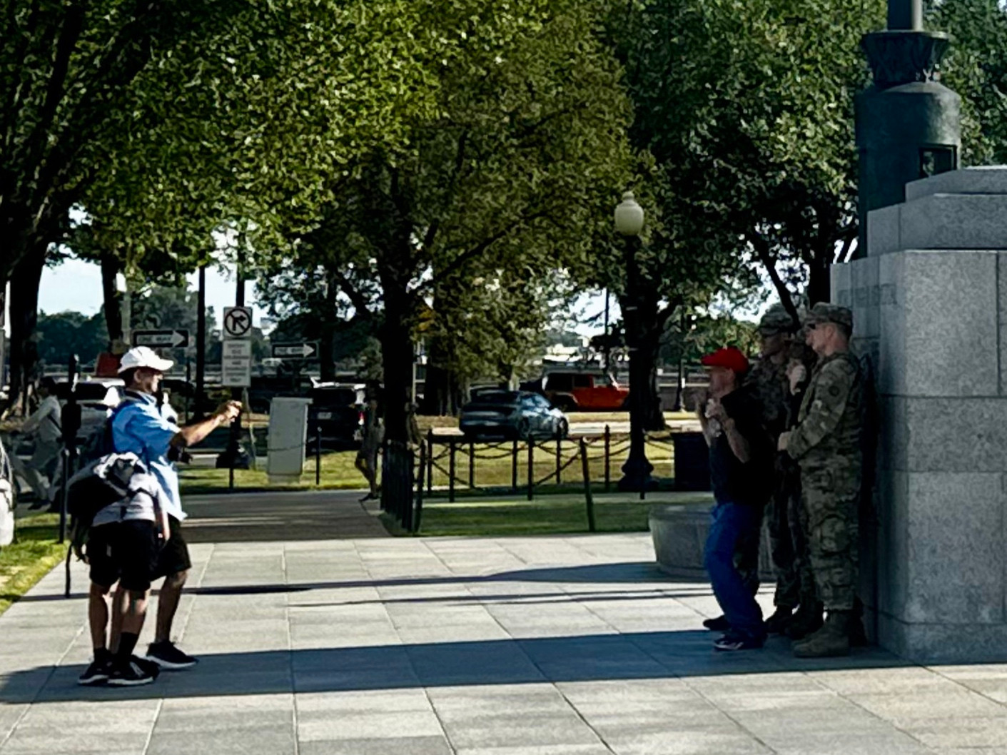 A guy in a hat and backpack takes a photo of national guardsmen in front of the WW2 memorial in DC 