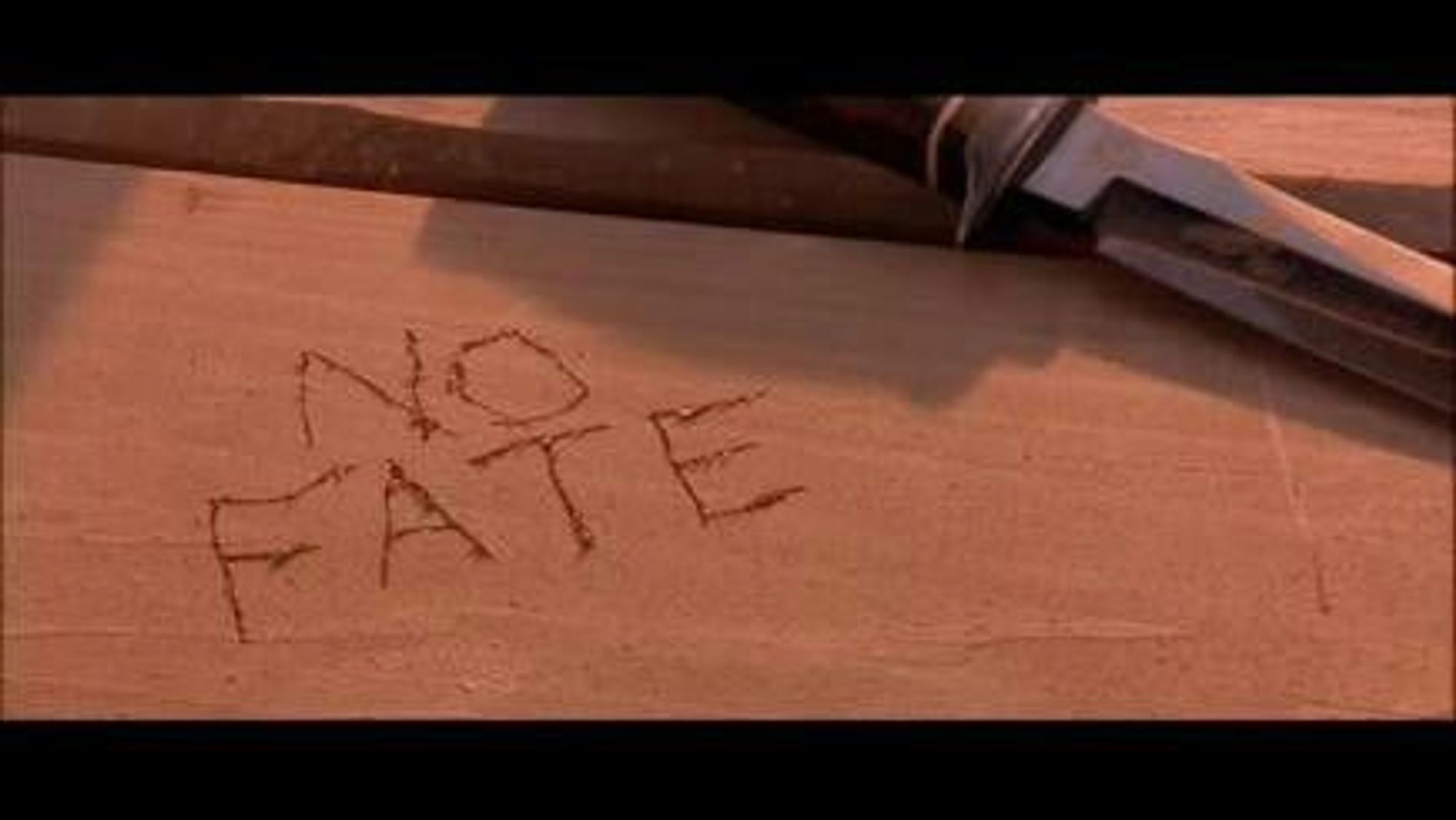 screenshot from terminator 2: judgement day. 
image is of the words "no fate" carved into the wood of a table in the desert.