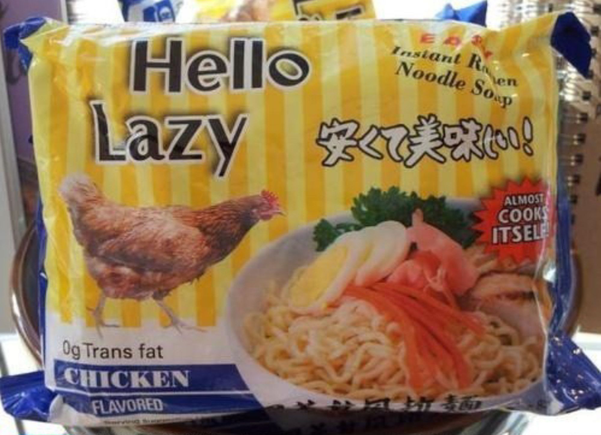 A pack of ramen with light and dark vertical yellow pinstripes called "Hello Lazy". It has some kanji with an exclamation point above a bowl of thesoup with a shrimp, chicken, sliced eggs, carrots, and garnish greens on it. A logo informs you it "ALMOST COOKS ITSELF!" A brown rooster to the left of the bowl is marching towards it, presumably to commit cannibalism. They would also like you to know this ramen has 0g trans fat.