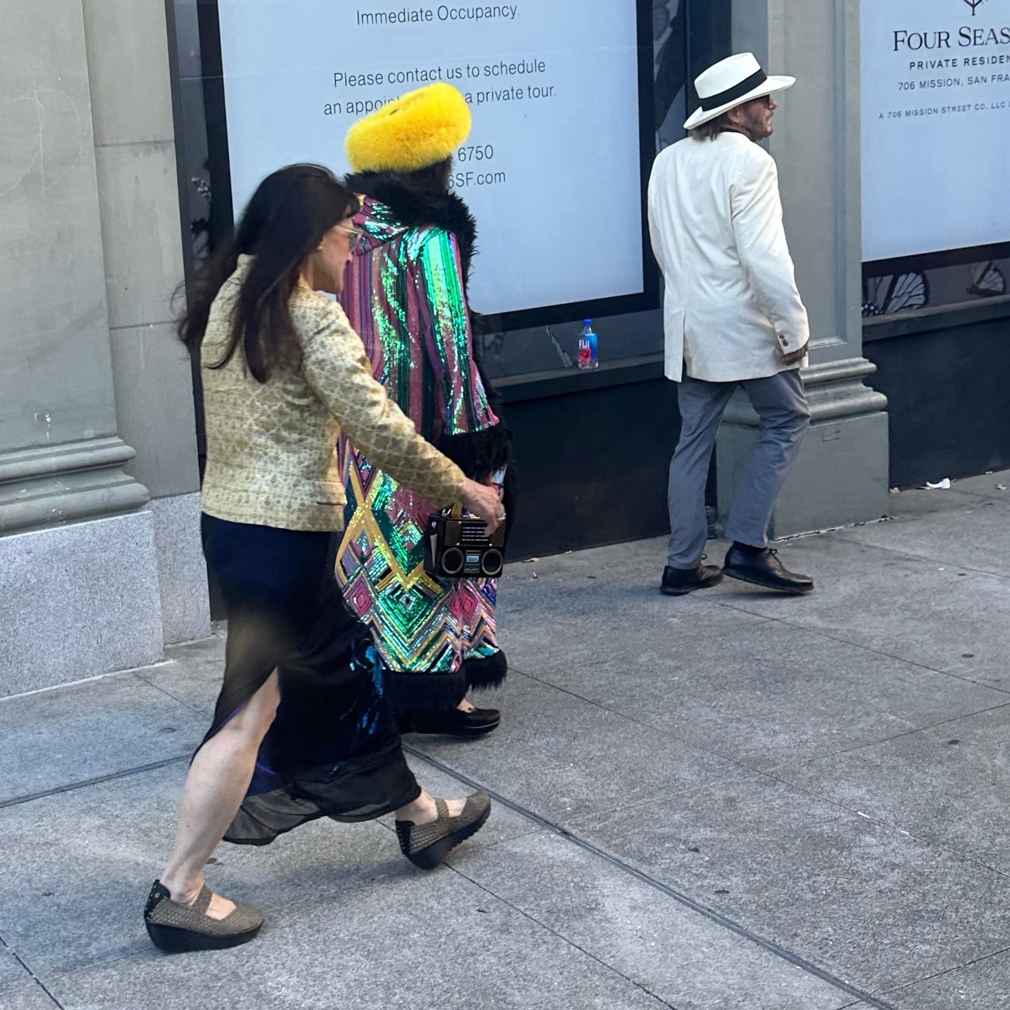 Trio of middle aged folks wearing an incredible embroidered oil slick sequined coat, a boom box trunk purse, a yellow Russian doll hat. The other two are wearing Panama hat and white linen coat, and midnight sequined gown with gold brocade jacket.