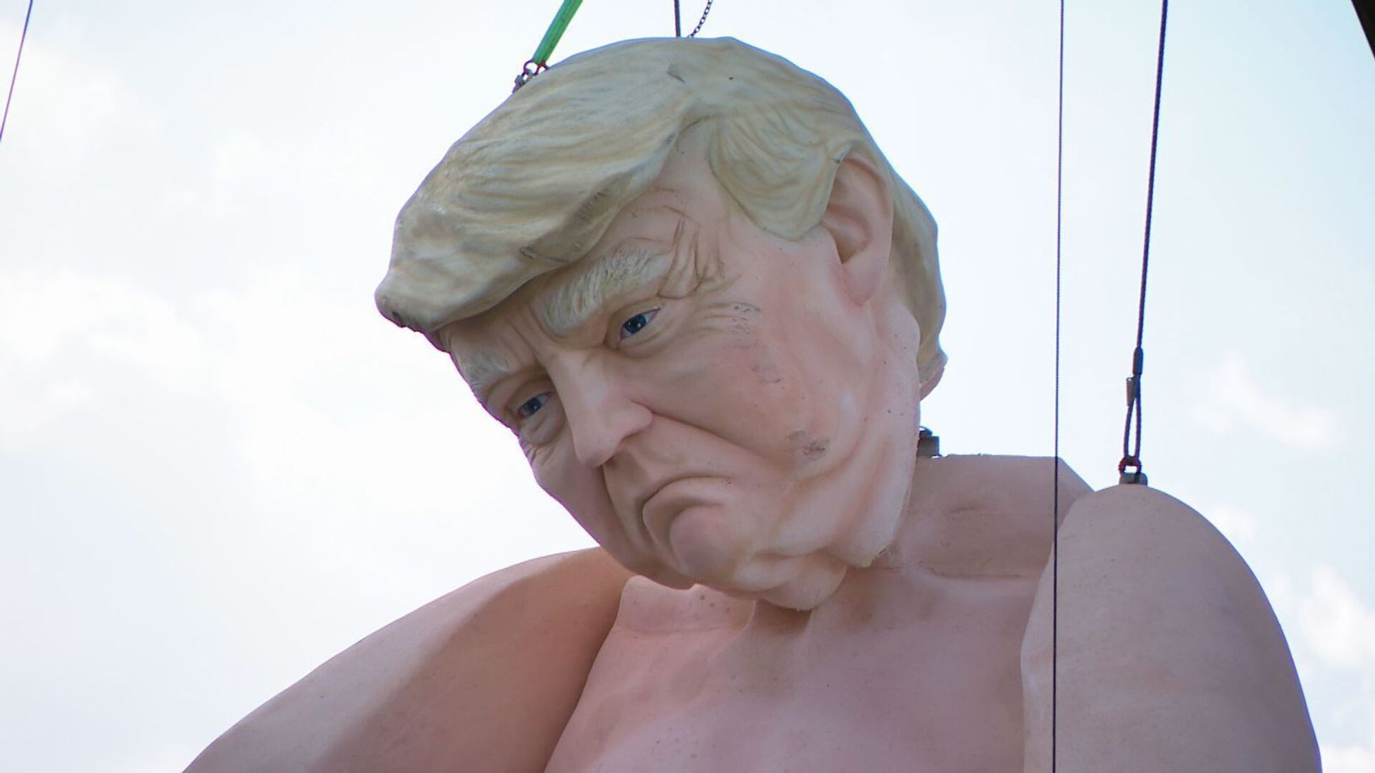 A large statue of a nude Donald Trump being hoisted by a crane