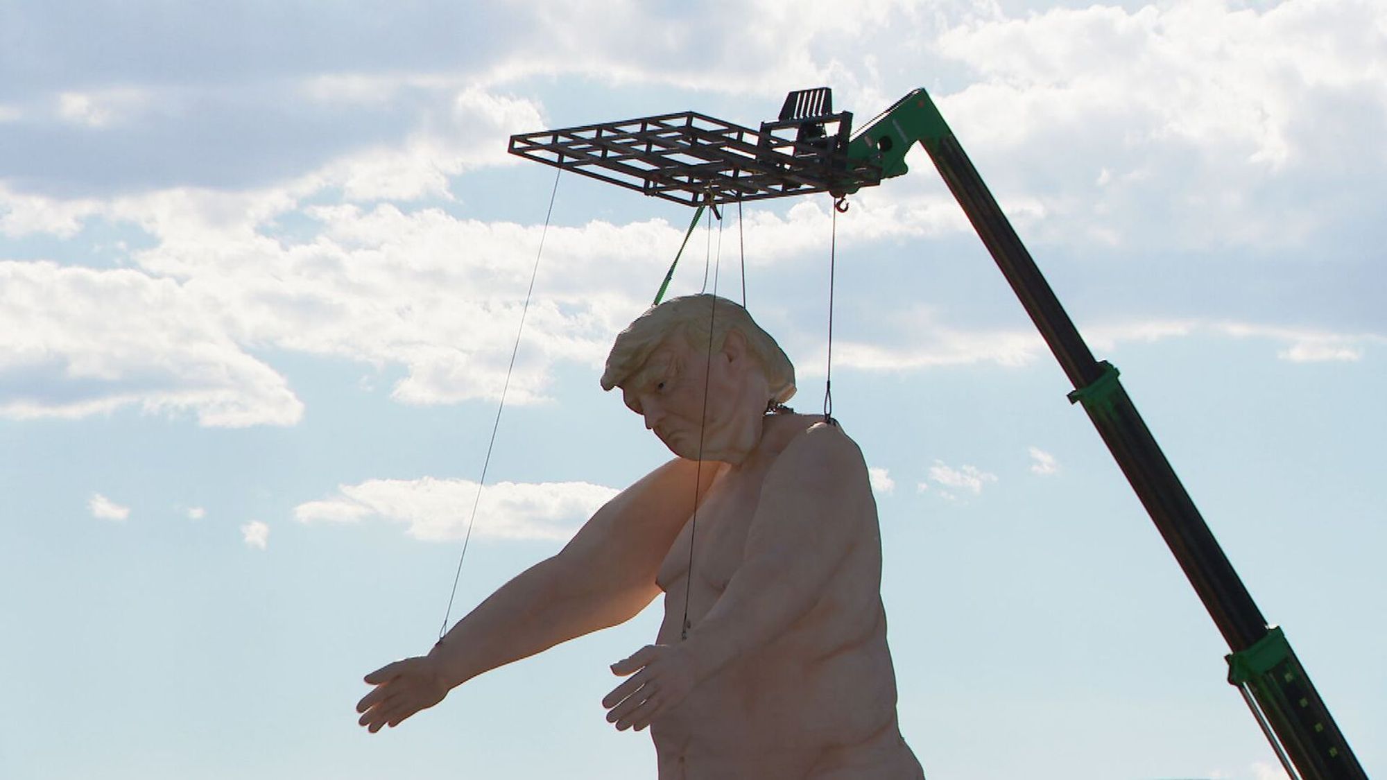 A large statue of a nude Donald Trump being hoisted by a crane