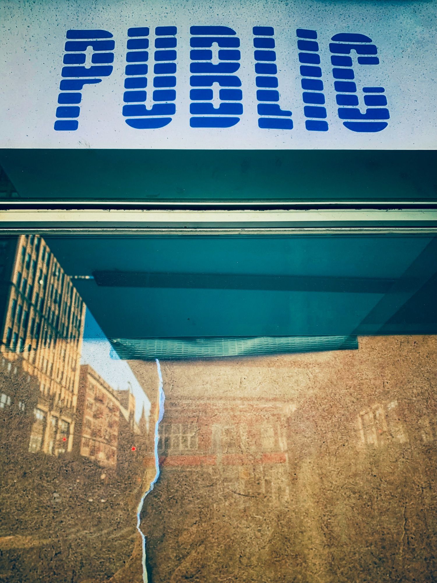 A sign saying “public” over a glass window. The window is reflecting city buildings.