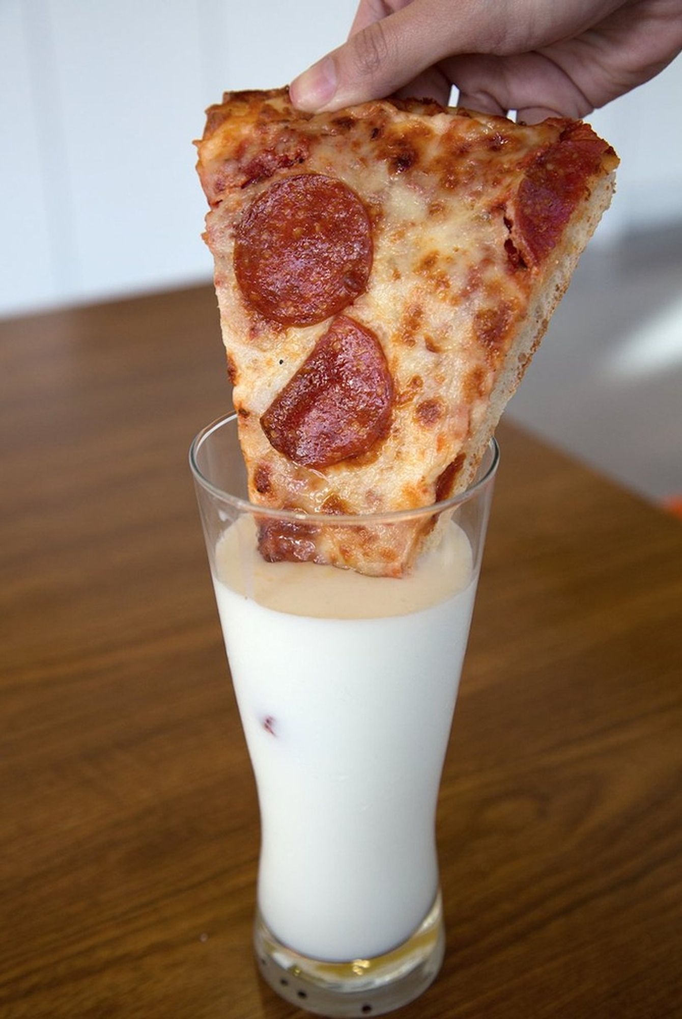 a slice of pepperoni pizza being dipped into a glass of milk