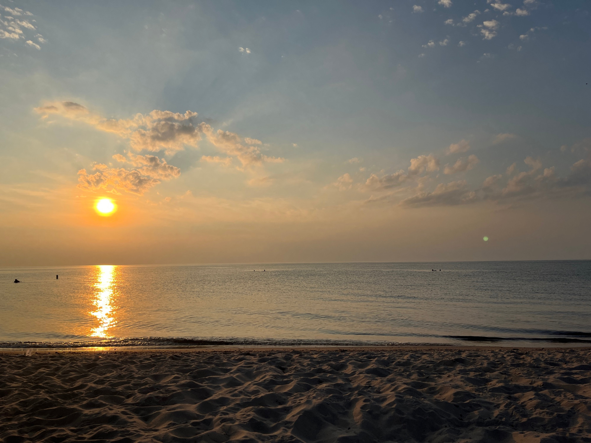 An orange sun setting over Lake Michigan, with a sandy beach in the foreground.