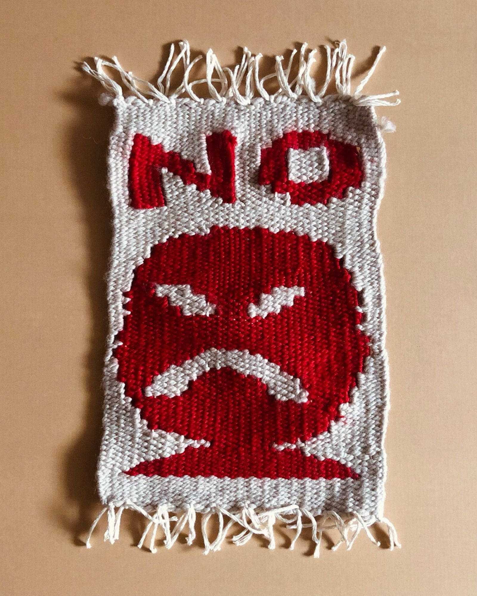 Poorly made weaving of an angry red face with the word NO.