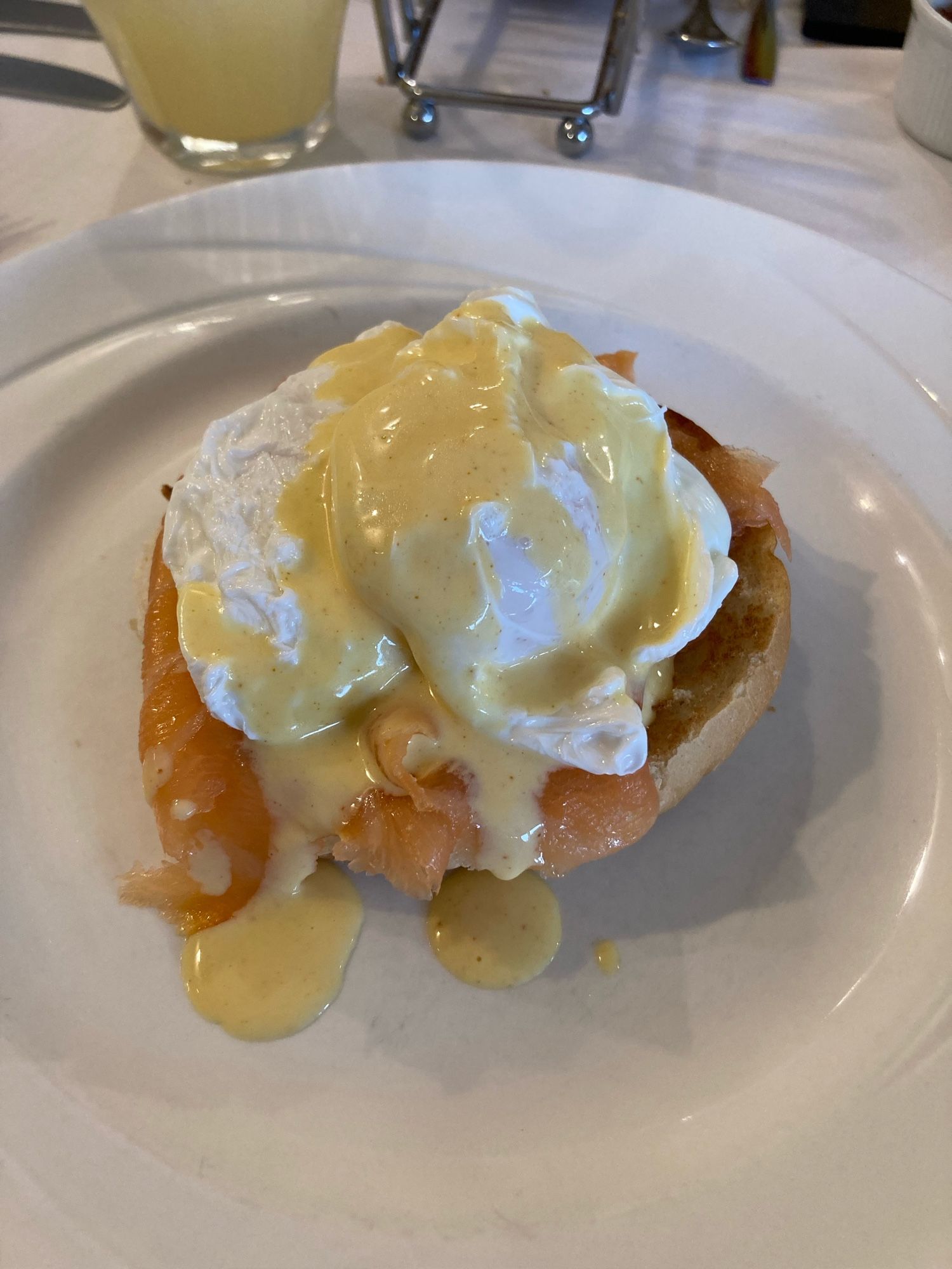 Auf einem weißen Teller liegt ein Stück geröstetes Brot, darauf Räucherlachs und ein pochiertes Ei. Das ganze mit Sauce Hollandaise übergossen.