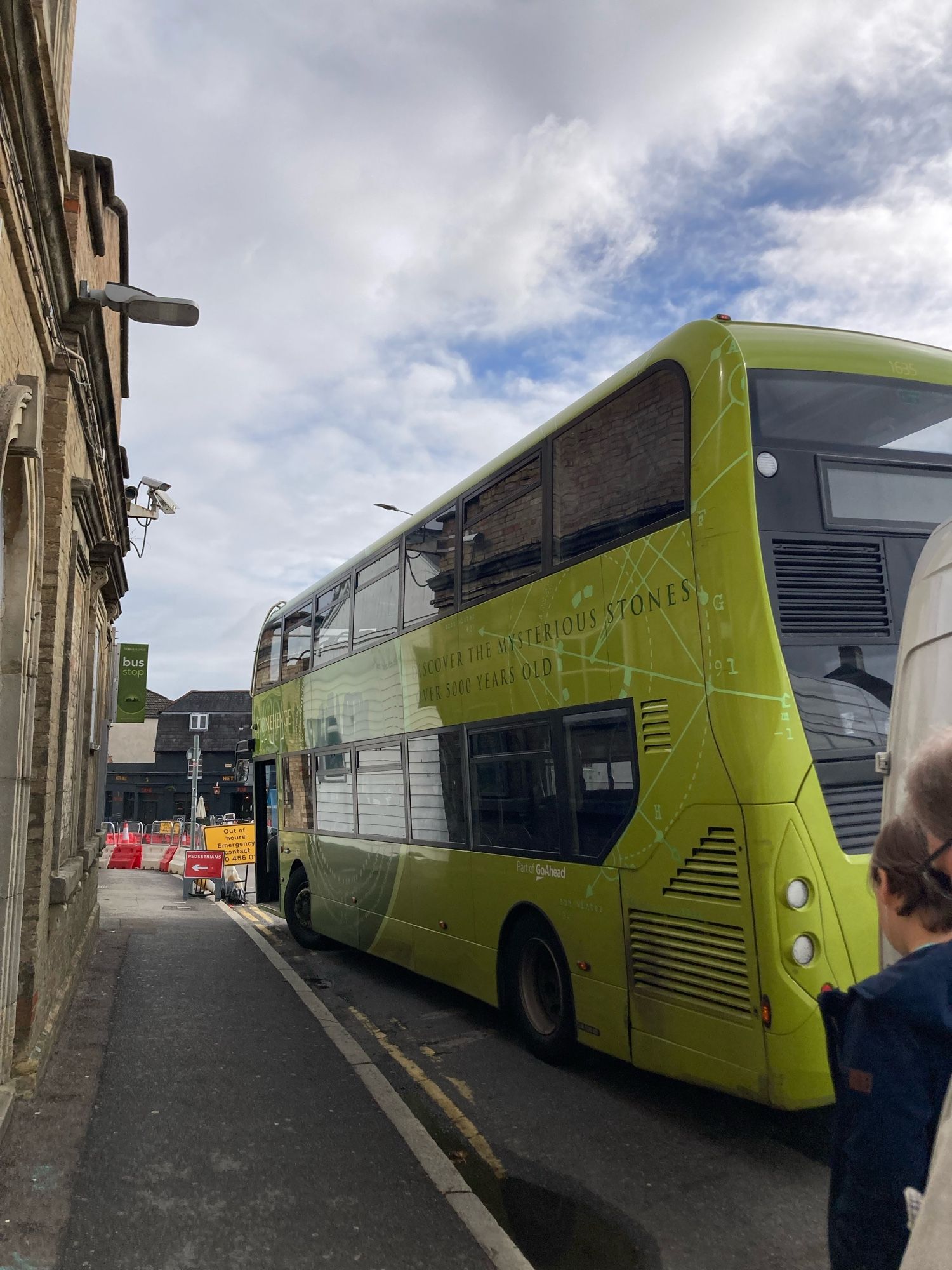 Ein hellgrüner Doppeldeckerbus steht am linken Straßenrand. Links eine Fassade.