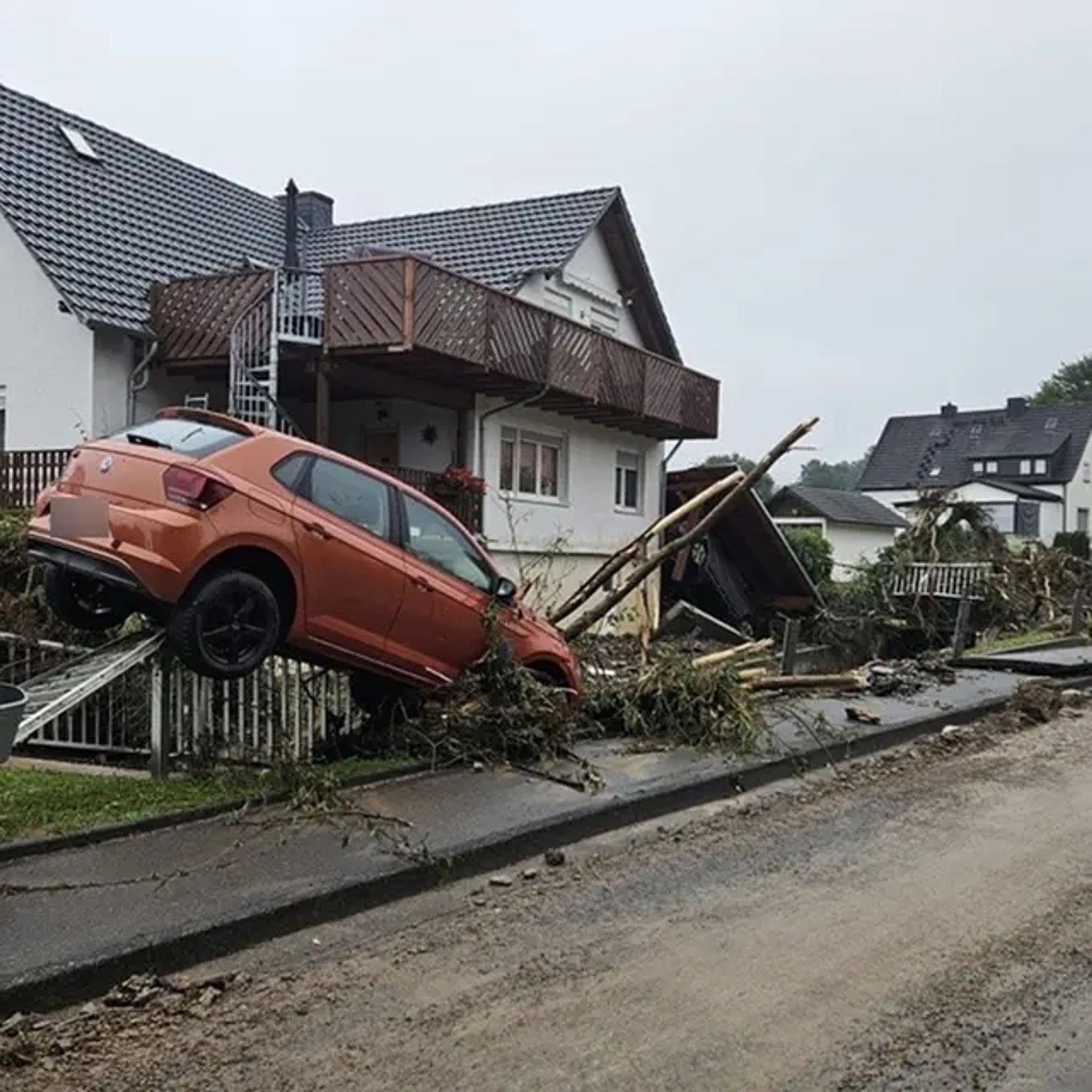 Im Hintergrund ein Haus im Vordergrund übereinander gestapelte Trümmerteile und ein Auto das auf einem Trümmerteil aufgespießt ist