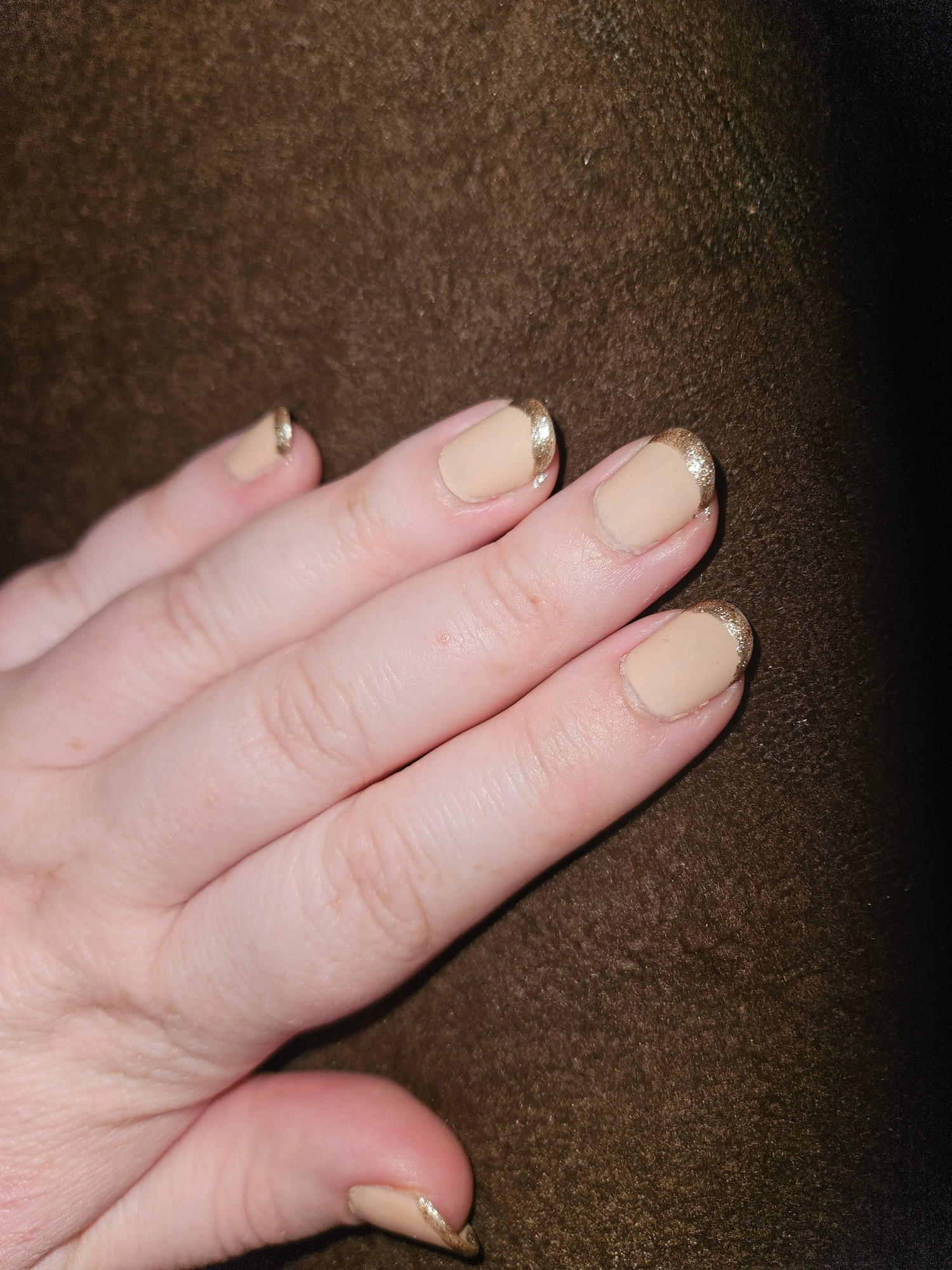 Pale skinned hand with nude nail polish with a gold French tip