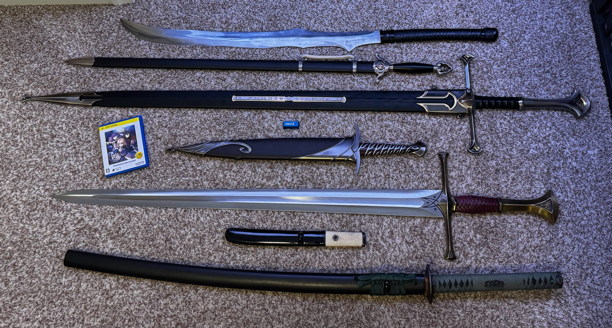 A collection of swords of various types and levels of functionality, joined by a PS Vita copy of Fate/Stay Night and a metal Excalibur keycap