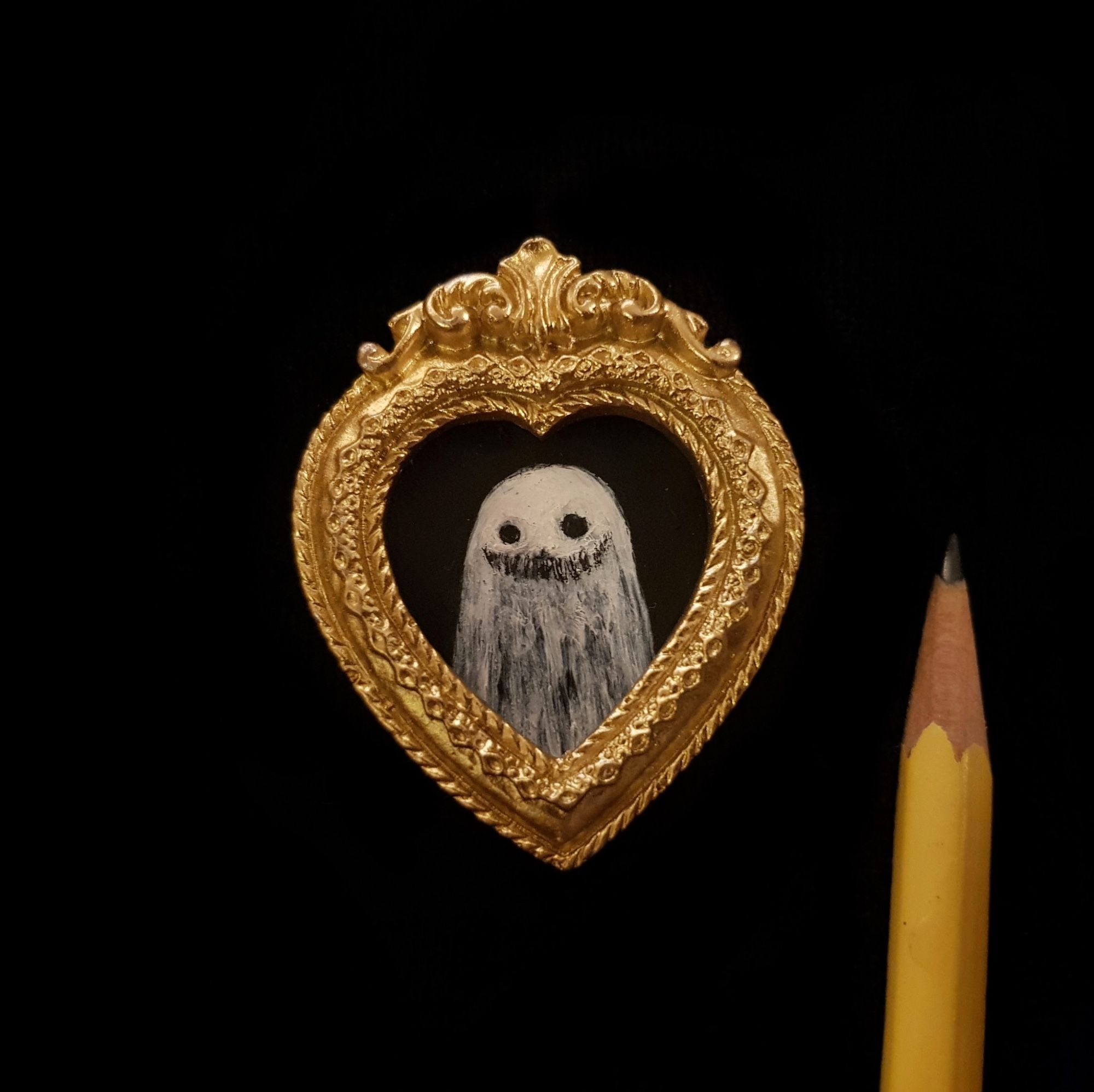 A miniature acrylic painting portrait of a ghost in a miniature gold frame, next to a pencil tip.