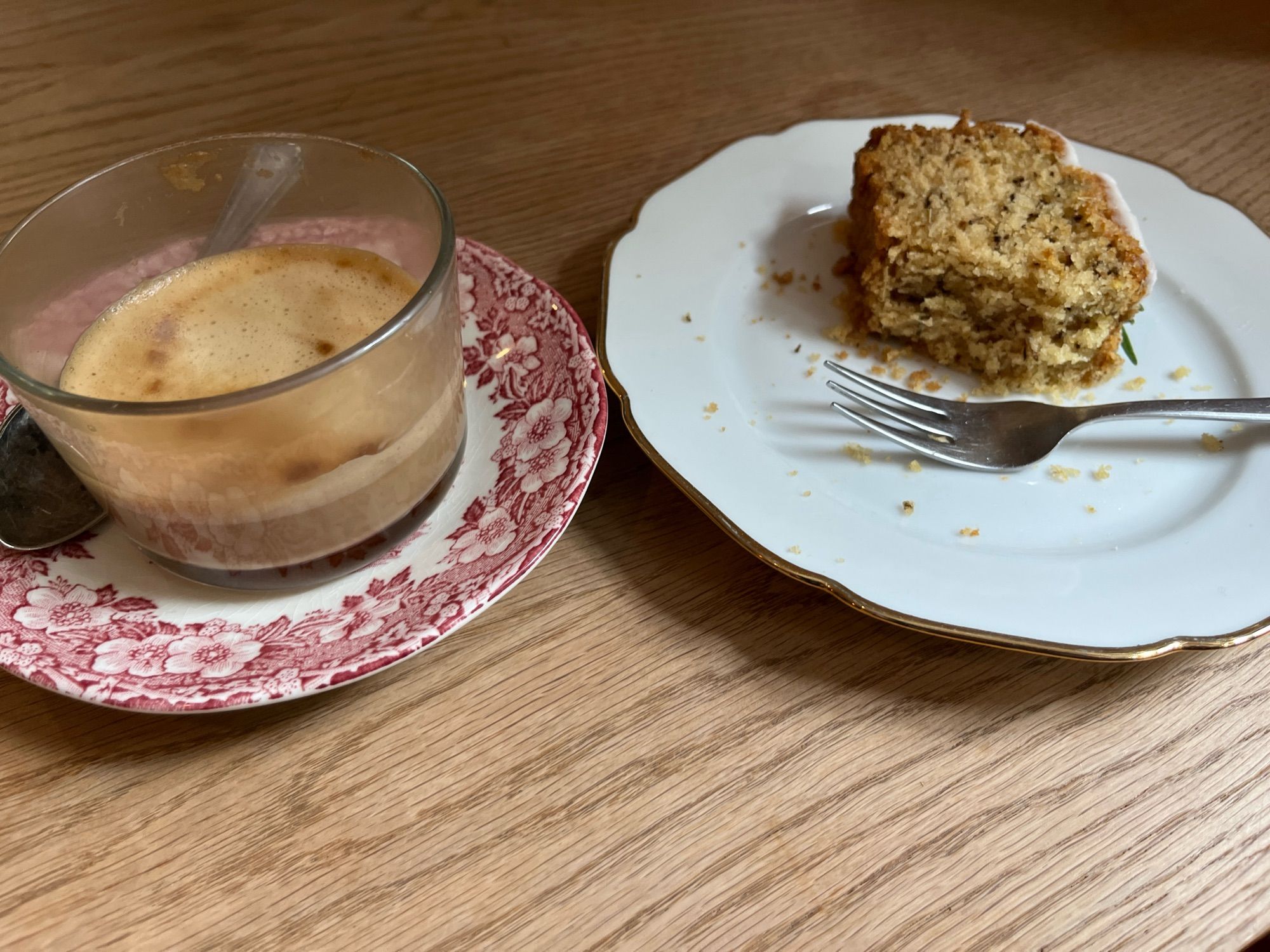 Das Foto zeigt einen Glasbecher mit Cappuccino und einen Teller mit Kuchen