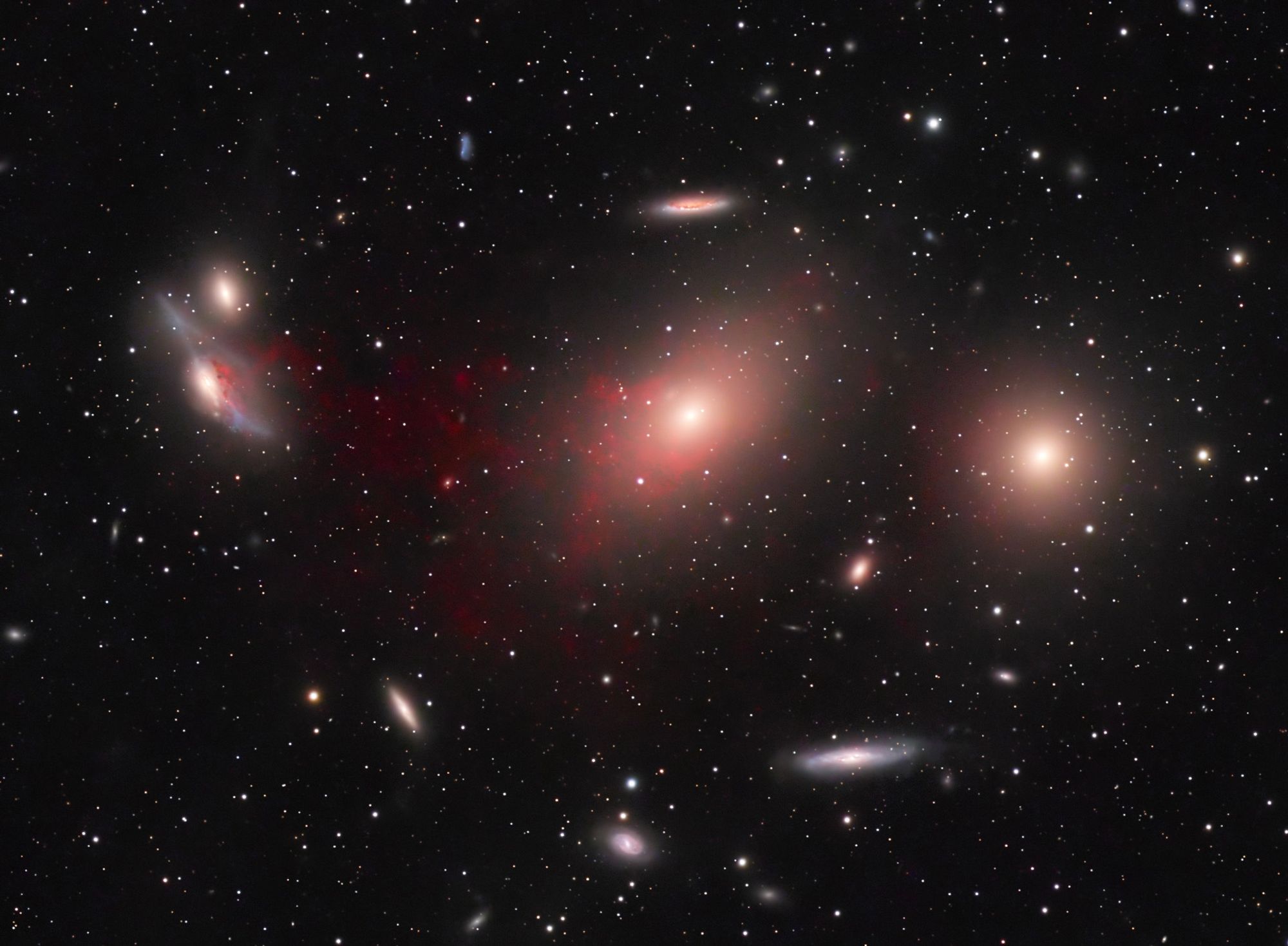 A close group of galaxies of various shapes, with a prominent red intergalactic hydrogen gas bridge resulting from a collision millions of years ago