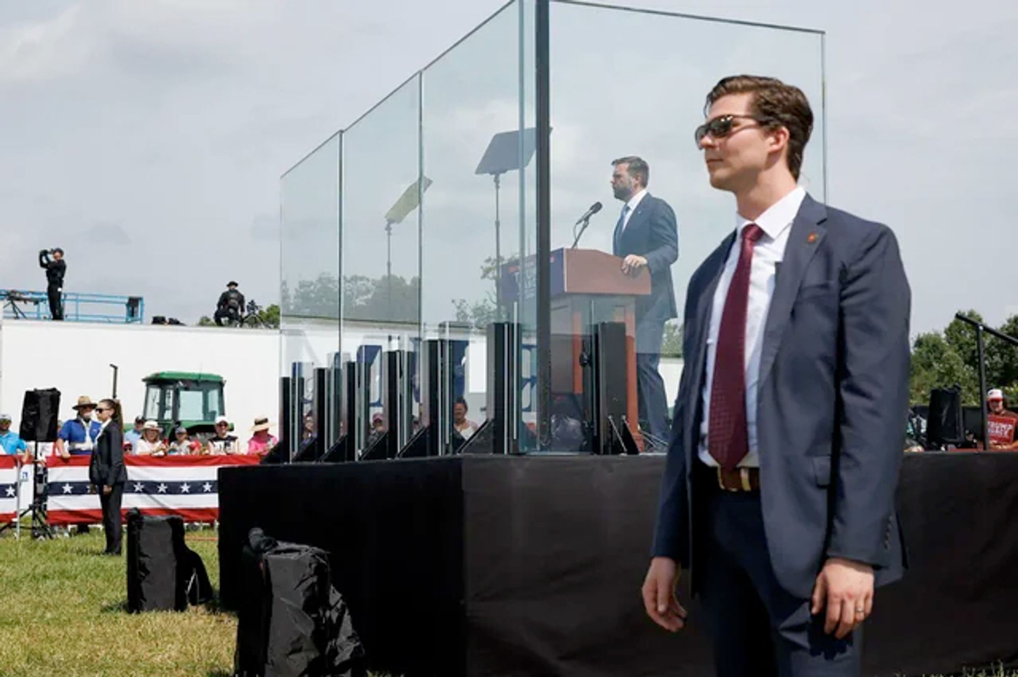 JD Vance speaking from behind bulletproof glass in Michigan