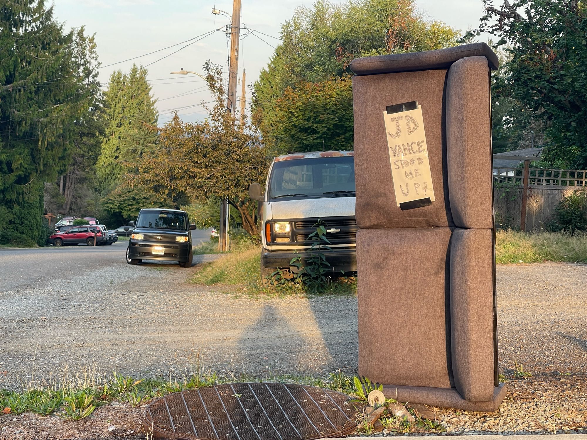 Abandoned beside the road, set on end. A hand written sign on the couch reads JD Vance stood me up.