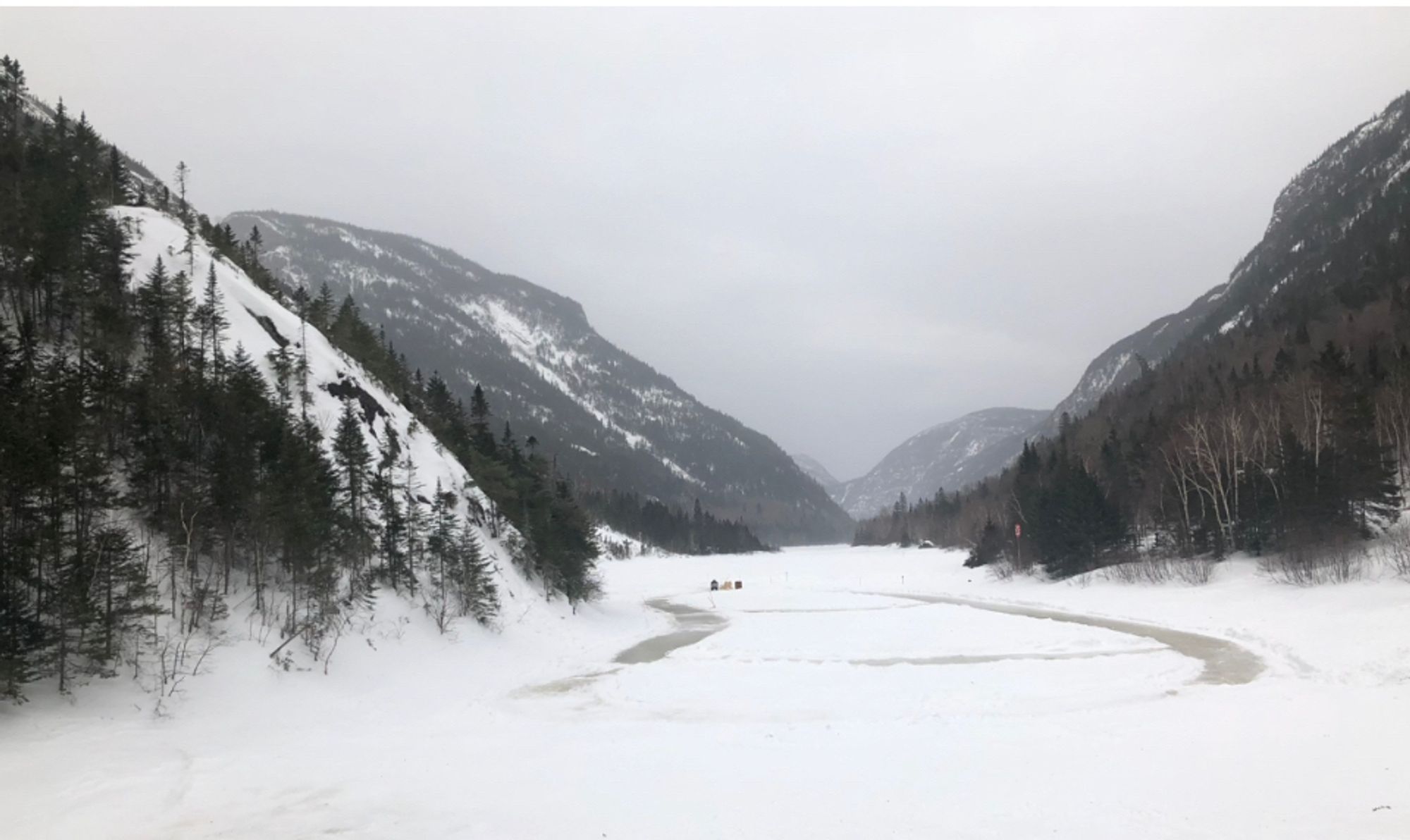 Grey mountains on each side of a river in a snowy landscape.