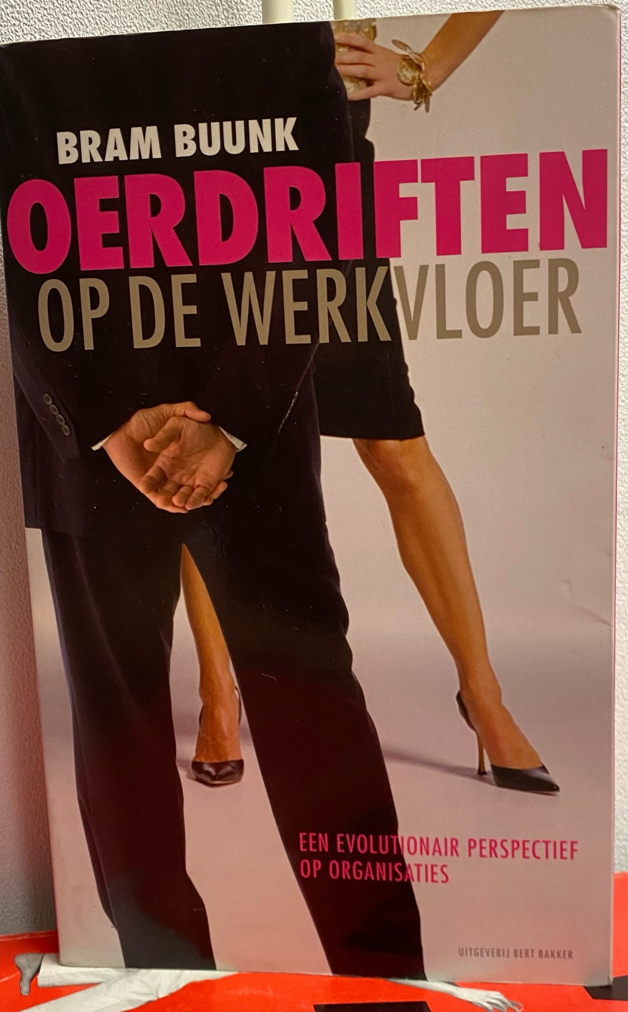 Boekomslag ‘Oerdriften op de werkvloer’. Je ziet een man in pak met de handen op de rug en twee vrouwenbenen (neem ik aan) met rok en naaldhakken.