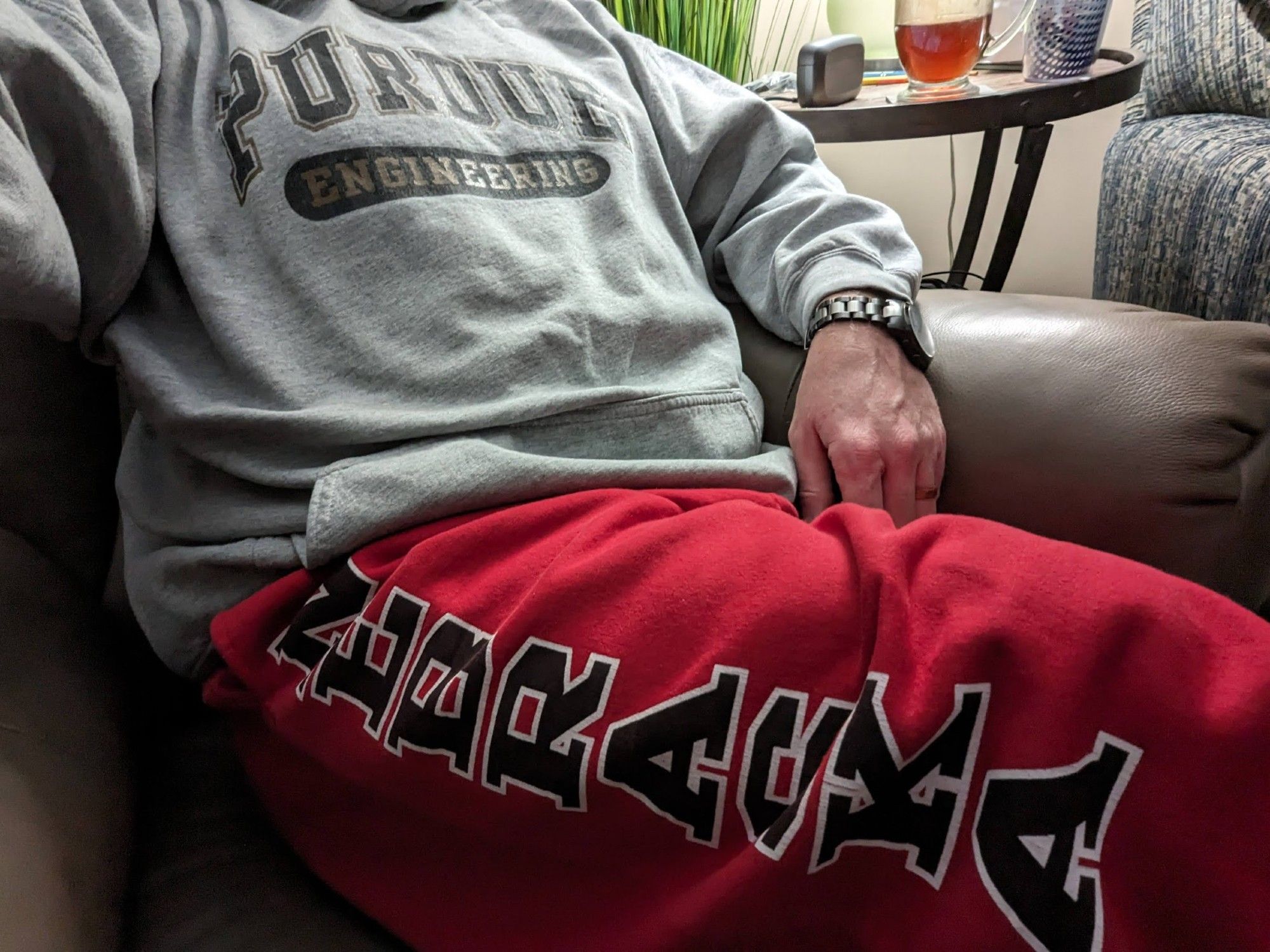 A man sitting in a reclining chair. He is wearing a gray sweatshirt labeled "PURDUE ENGINEERING" and red sweatpants labeled "NEBRASKA".