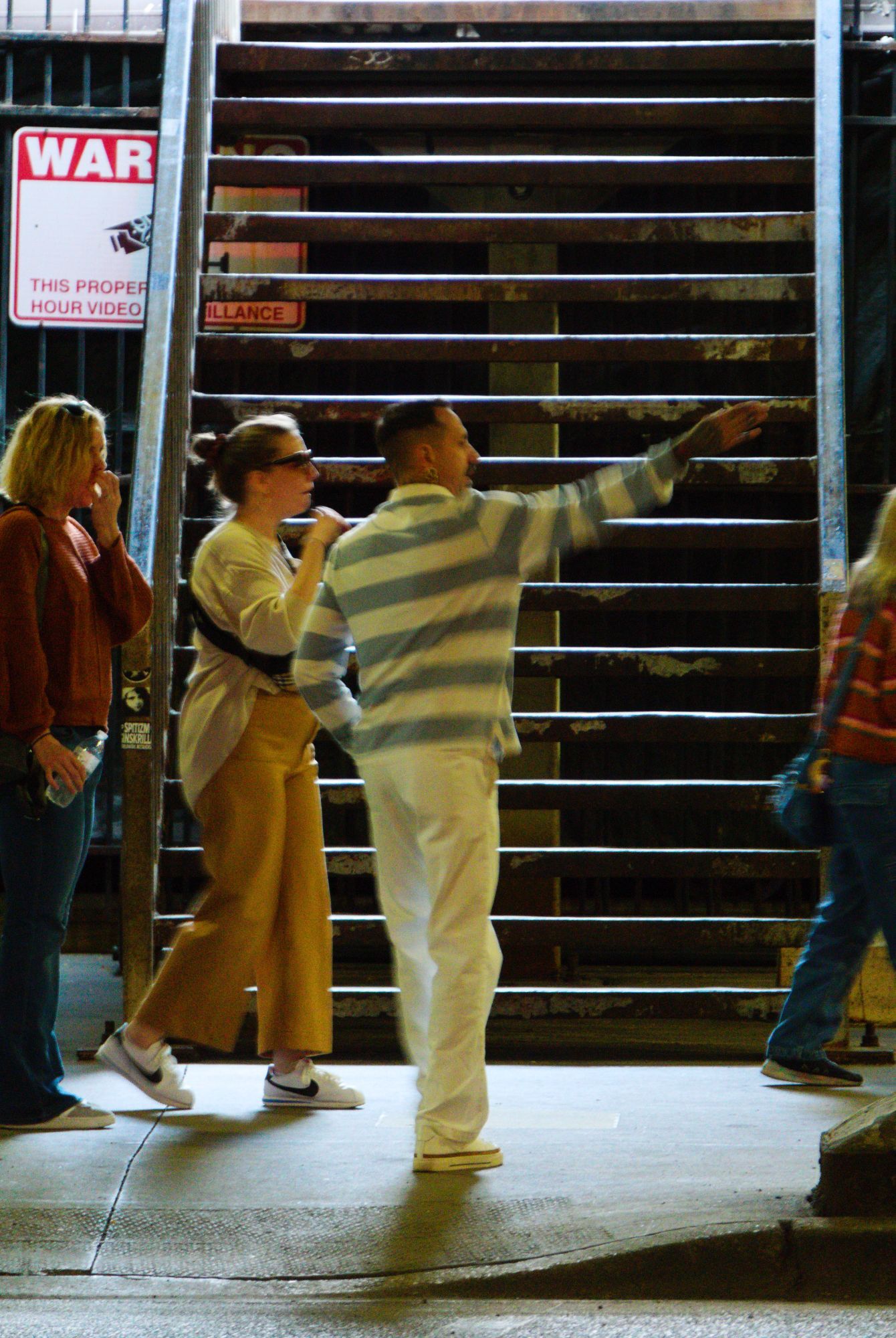 We're under Michigan Ave in all these shots. Using a 50-200mm (ish) lens, so we can snap some shots unobtrusively from half a block down. Here we're looking at the base of a staircase from this lower level, up to the main tourist section of Michigan Ave. A man in a white and green striped shirt is pointing off to the right, presumably giving directions for two or three middle aged women. Behind him, the horizontal lines of the stairs play nicely against the horizontal lines of his shirt. 