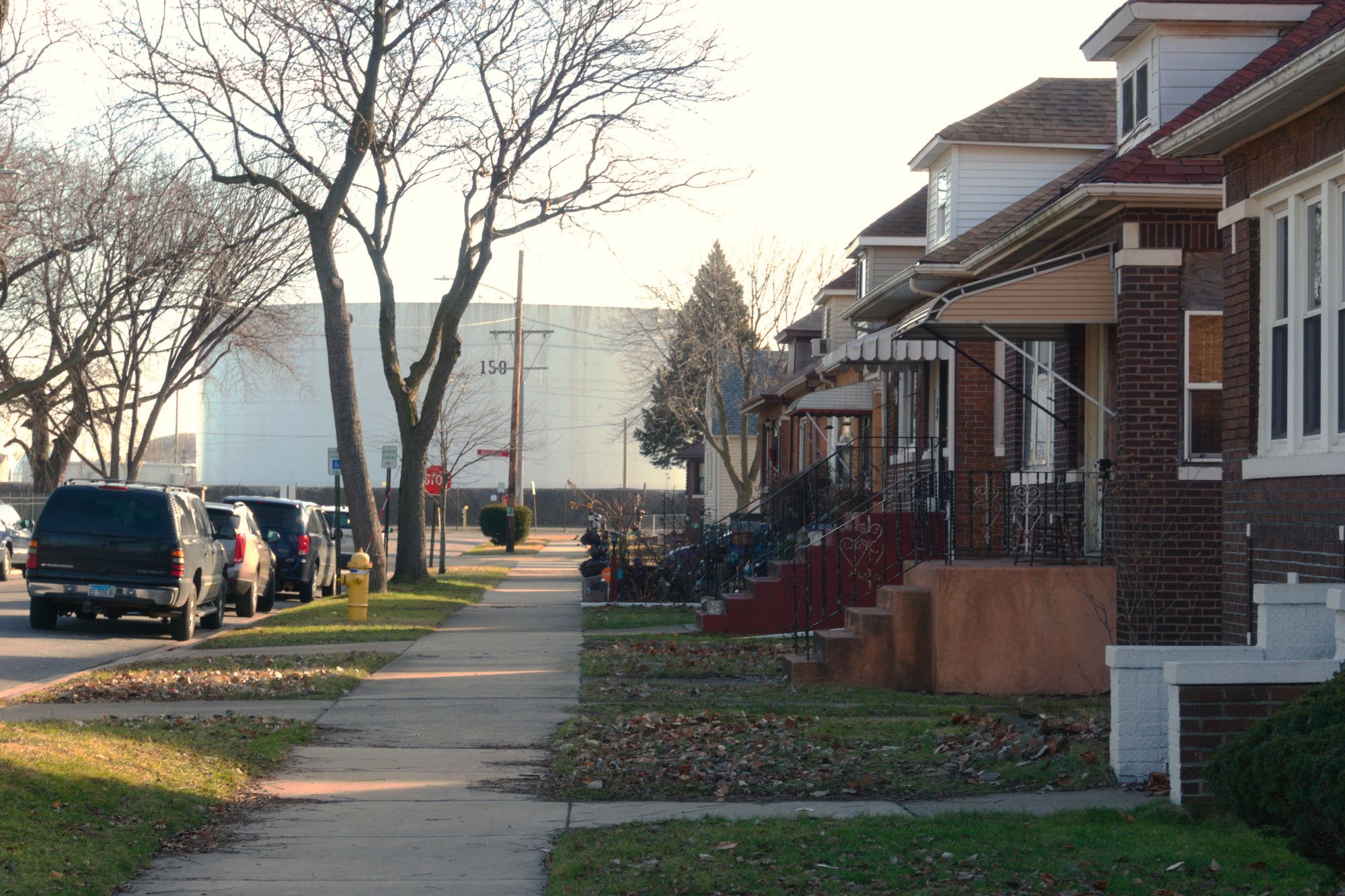 Here we're standing on a sidewalk on a residential block. On the right are half a dozen bungalow houses. At the end of the block, again, we see these cylindrical white petrochemical storage buildings. They must be less than 40 feet from the building at the end of the block.