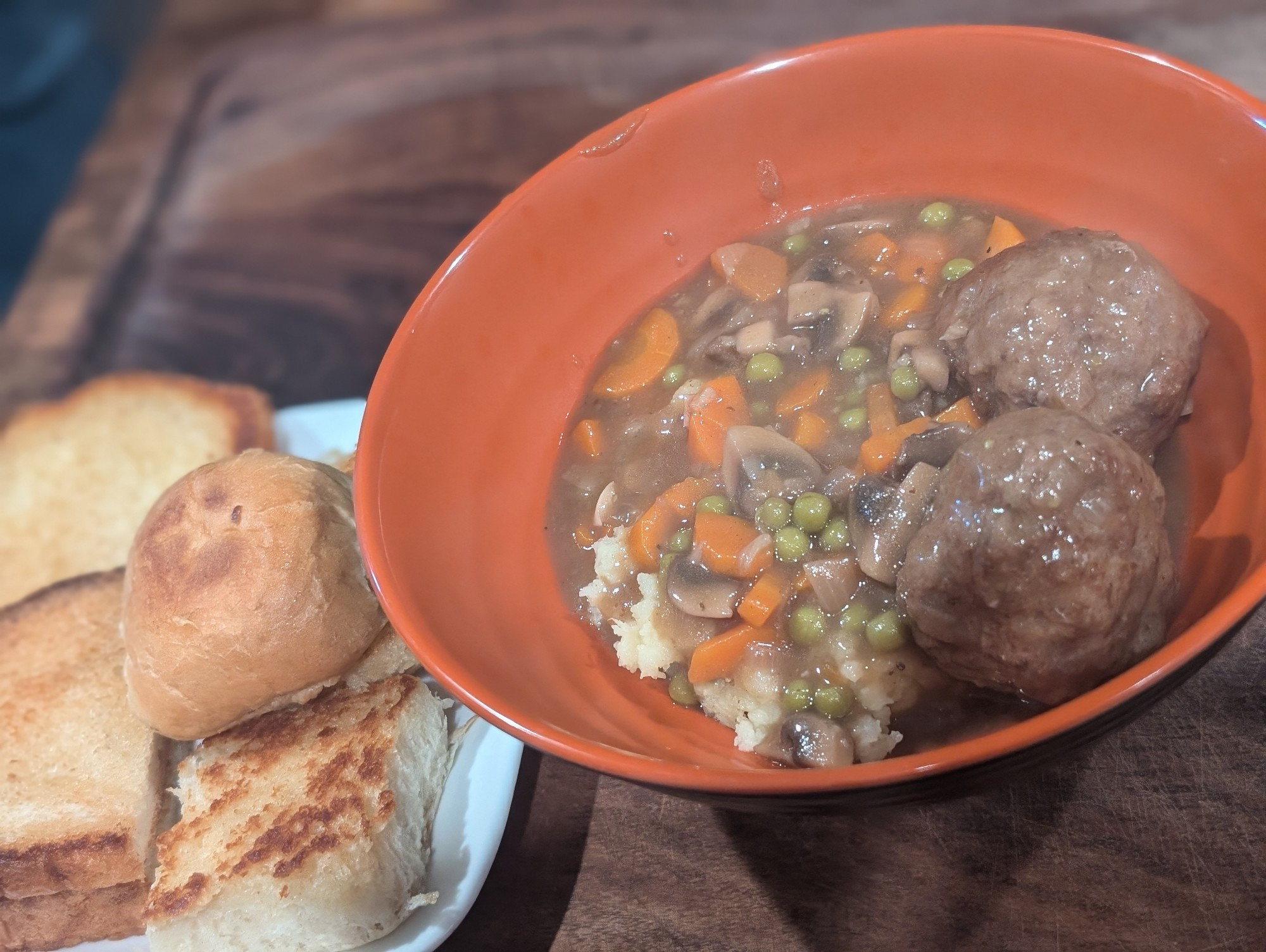 Photo of a plate of buttered, fried bread on the left and an orange bowl of meatball stew on the right