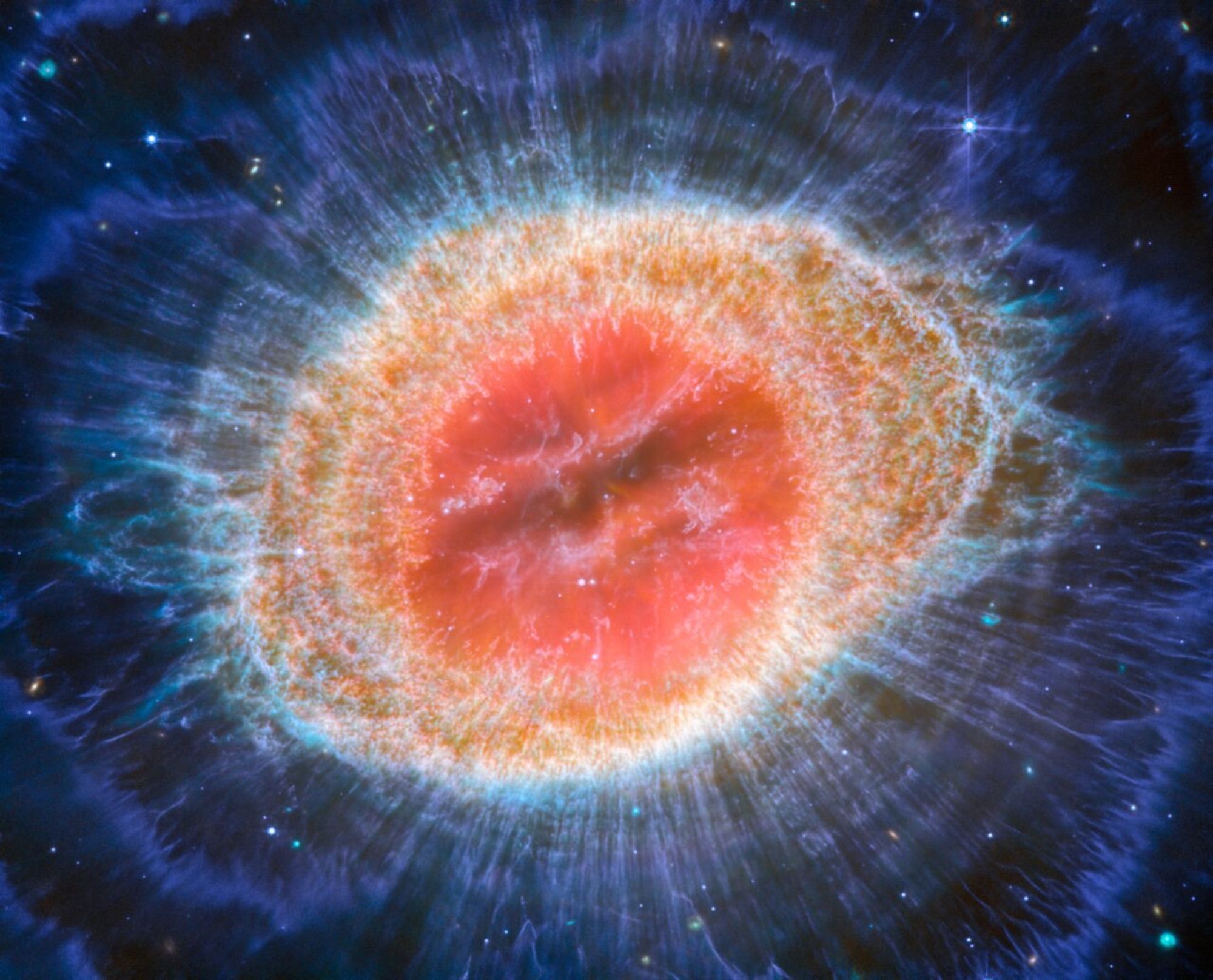 picture of the Ring nebula taken with the JWST observatory. the nebula is slightly oval in shape, red in the centre with some filamentary structure. The core is surrounded by an orange shell with intricate fine structure, evolving into thin deep blue wispy streamers and shells around it.