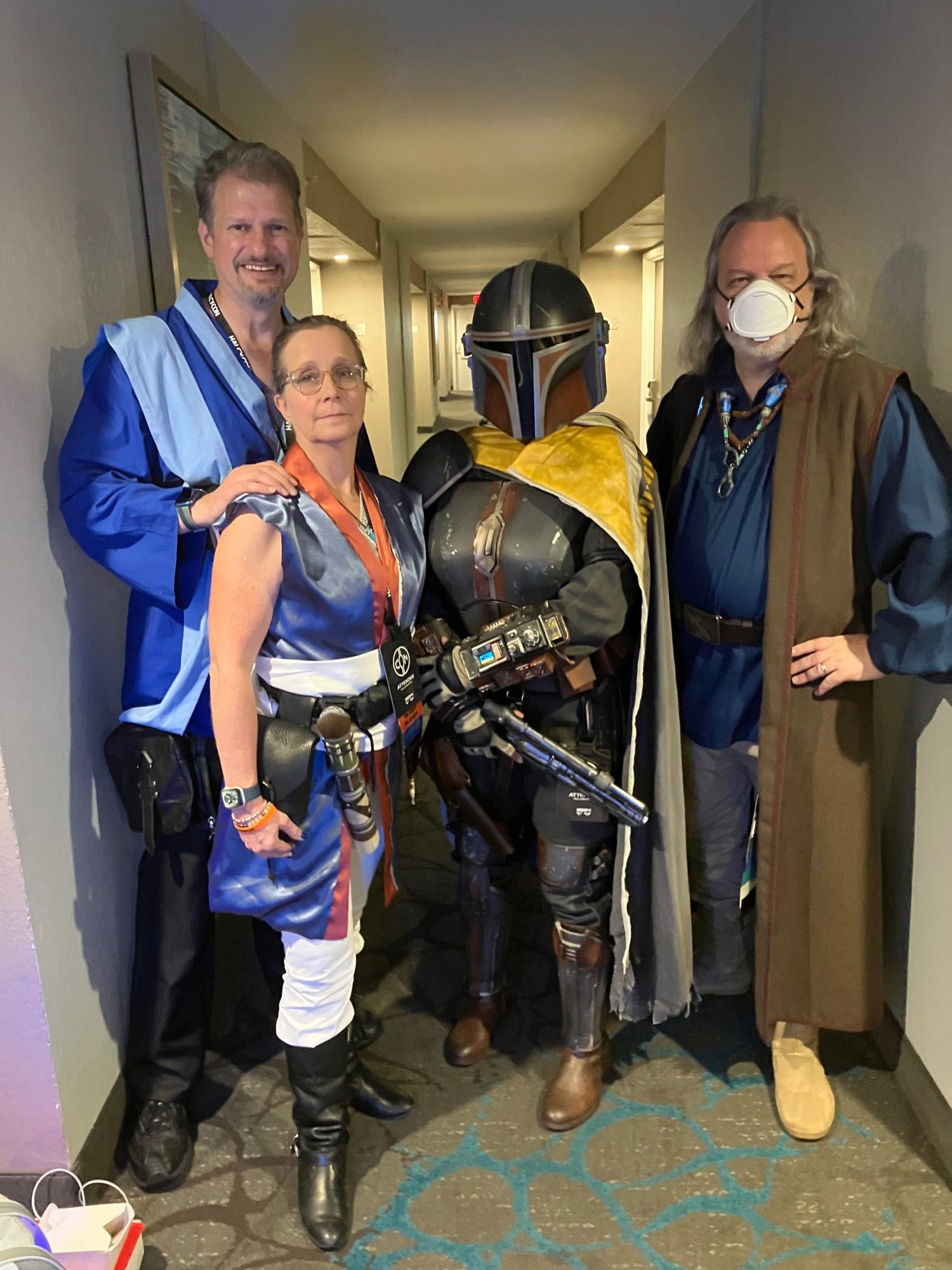 Four fans in a hallway; two in blue Jedi robes of their own design, one custom Mandalorian, and myself in a sort-of re-creation of Max von Sydow’s costume from The Force Awakens.