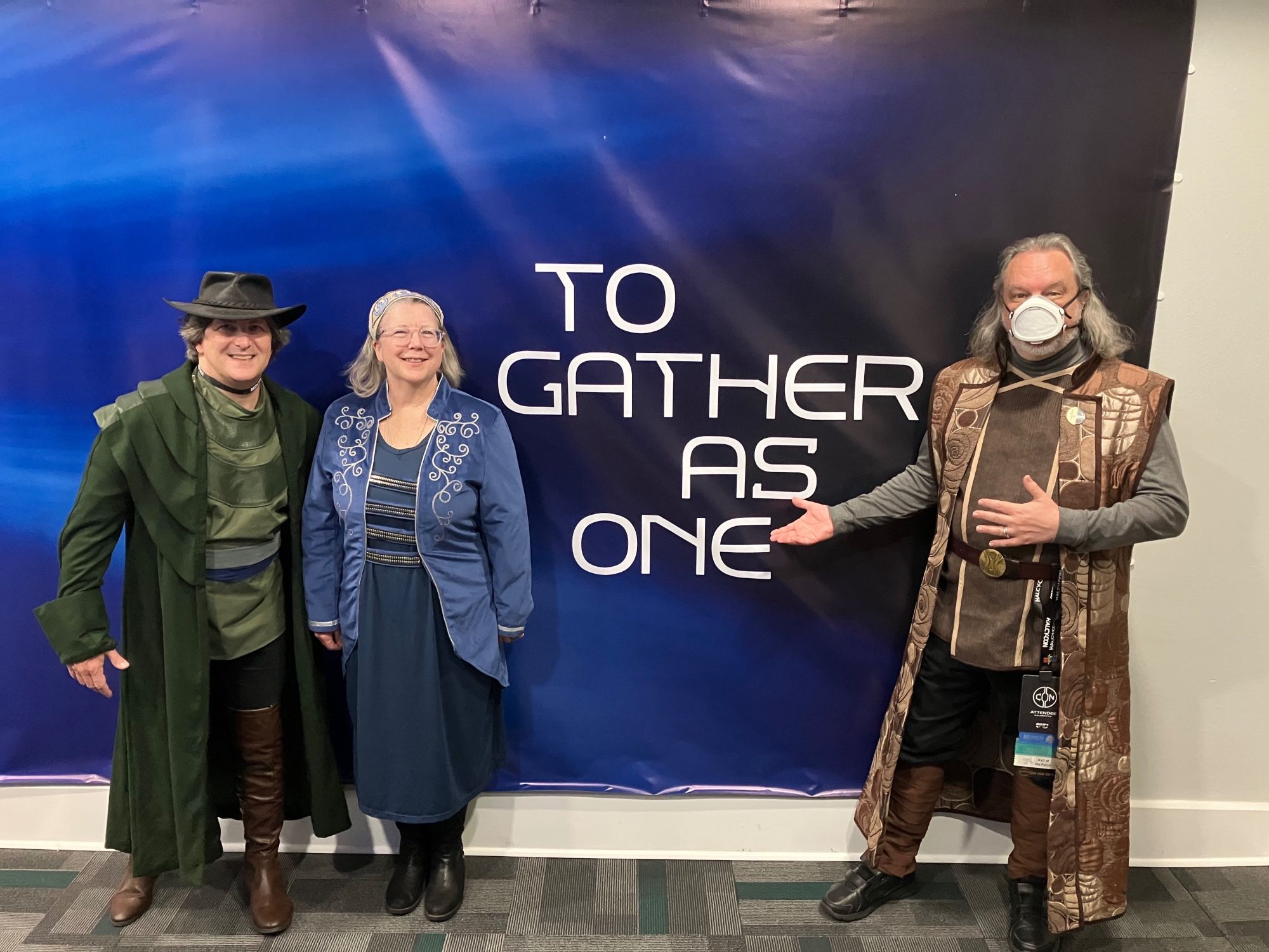 Two of my traveling companions and myself, in front of the “To Gather As One” backdrop (“Together!” “As one!” was a call-and-response refrain from the Starcruiser experience. We heard it a lot over the weekend). I’m in a very fancy sleeveless surcoat in brown metallic tones, over a brown vest with tan trim and grey shirt — actually the only completely original costume I wore at the con.