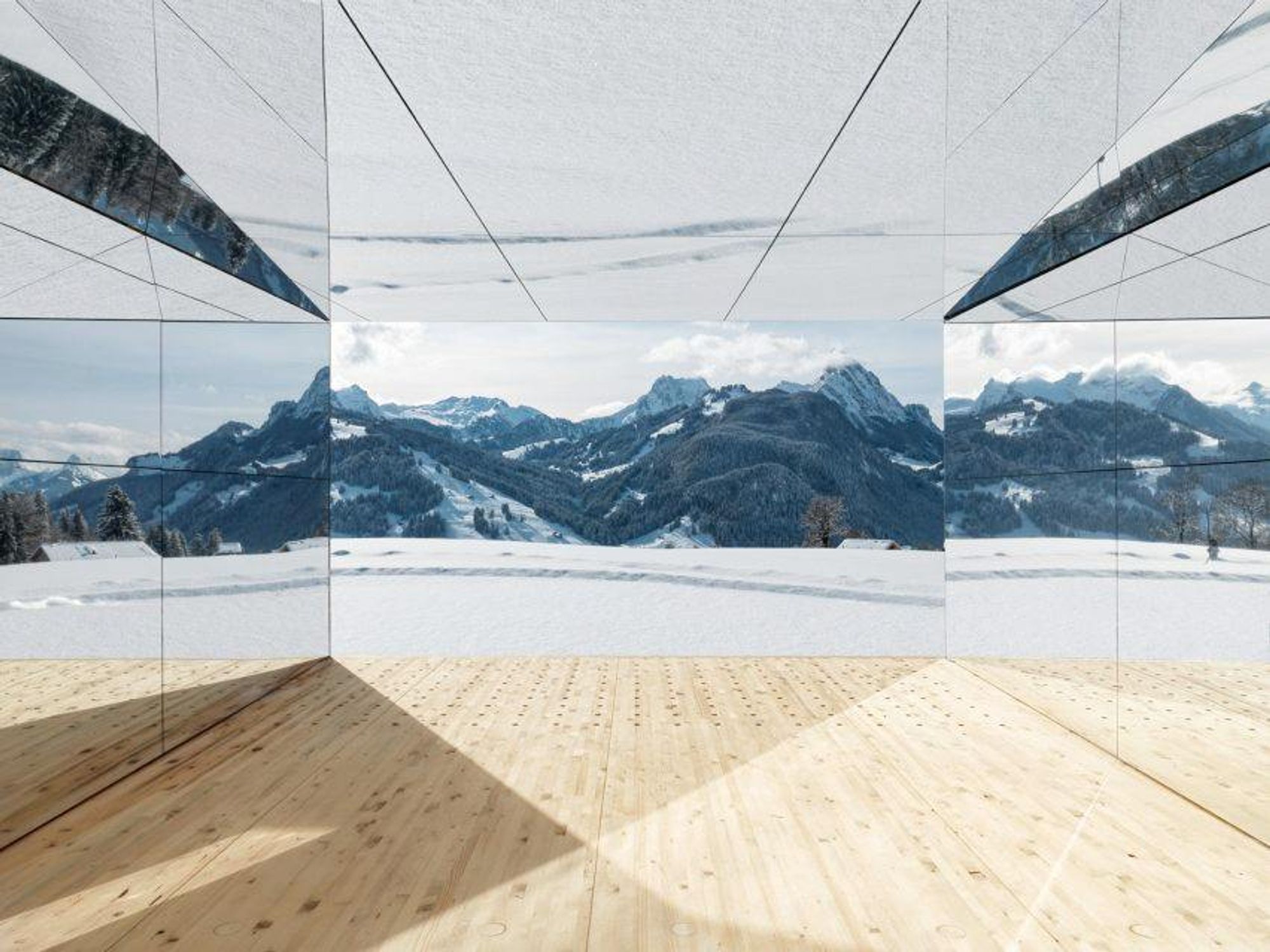 The interior of the house made of mirror (except the parquet floor) reflects the outdoor landscape: you see snowy mountains at the centre of the picture