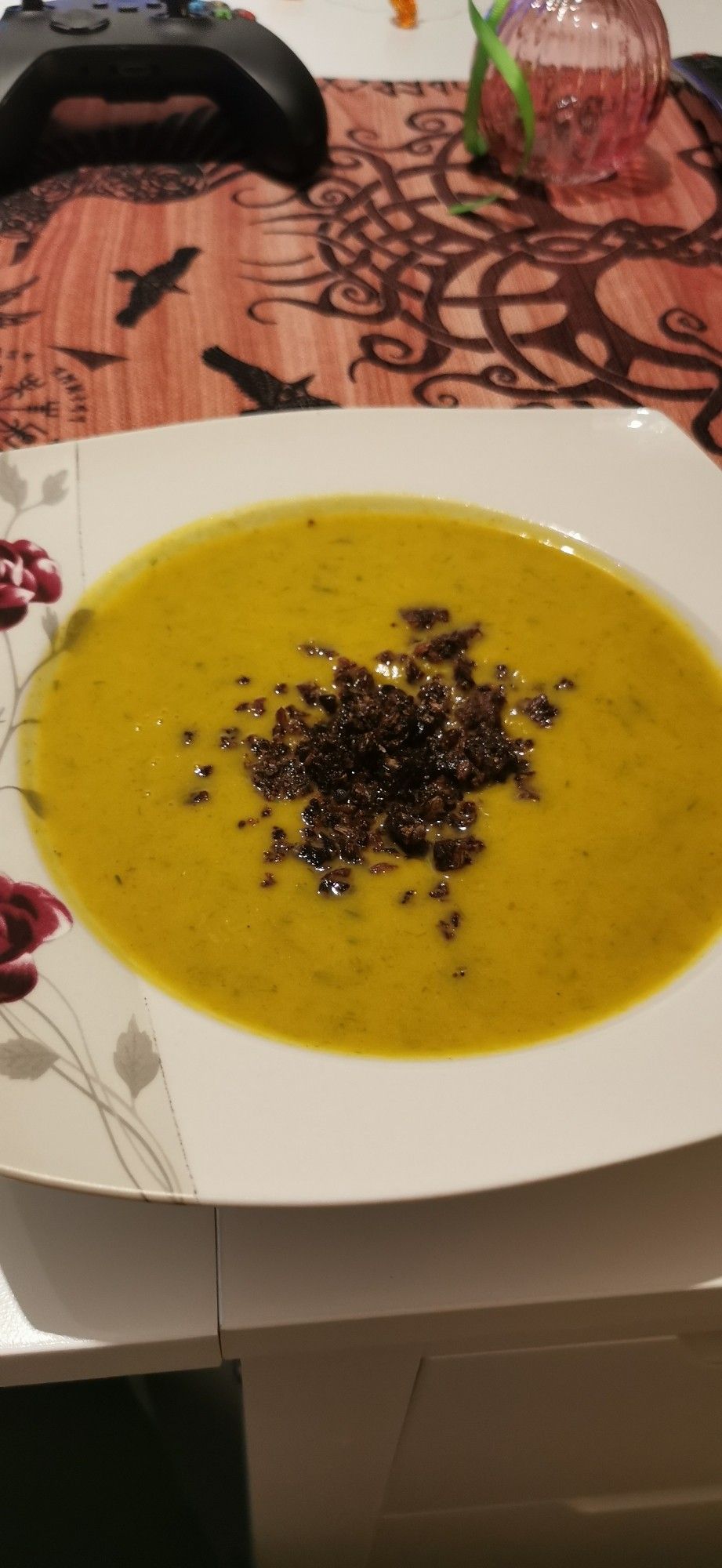 Ein Teller Cremesuppe in einem hellem orangeton steht auf einem weißen Tisch. Dunkelbraune geröstete Brotkrümel sind als Topping auf der Suppe