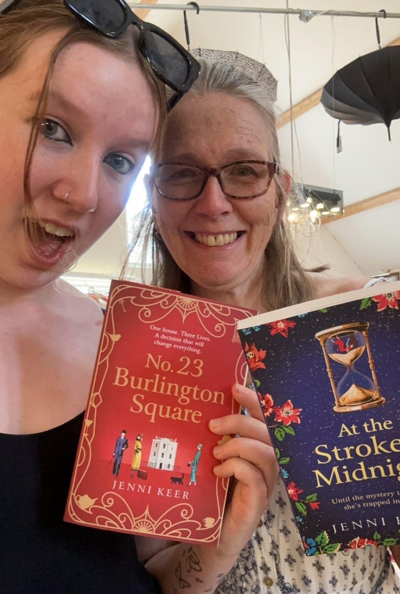 Two ladies, each holding a paperback book. One has a blue cover, the other red.