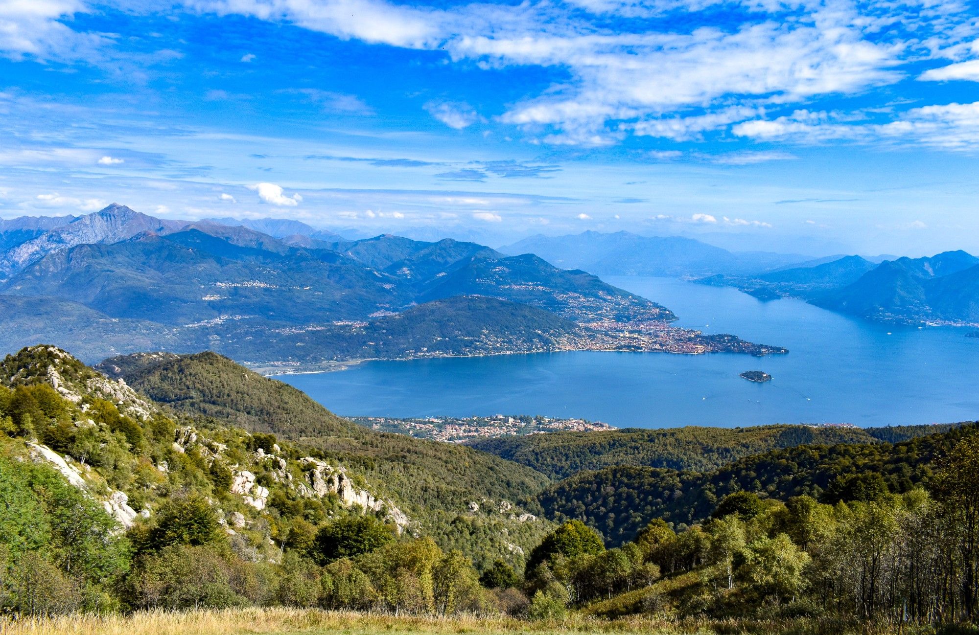 A wide view of Lake Maggiore in the Italian mountains under a blue September sky.