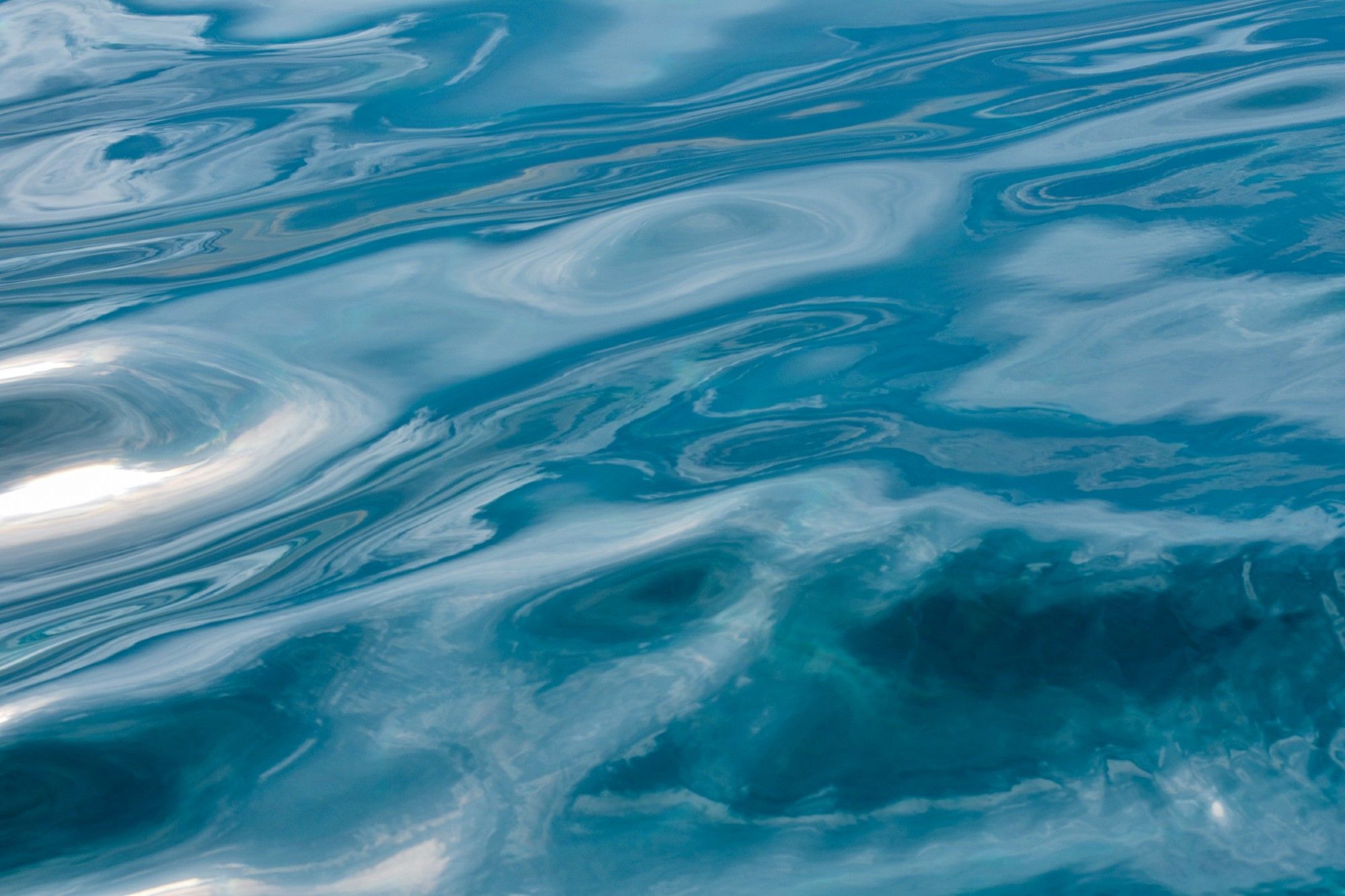 The deep blue sea, seen as a gentle, soft, unbreaking wave with the reflection of the bright sky giving depth.