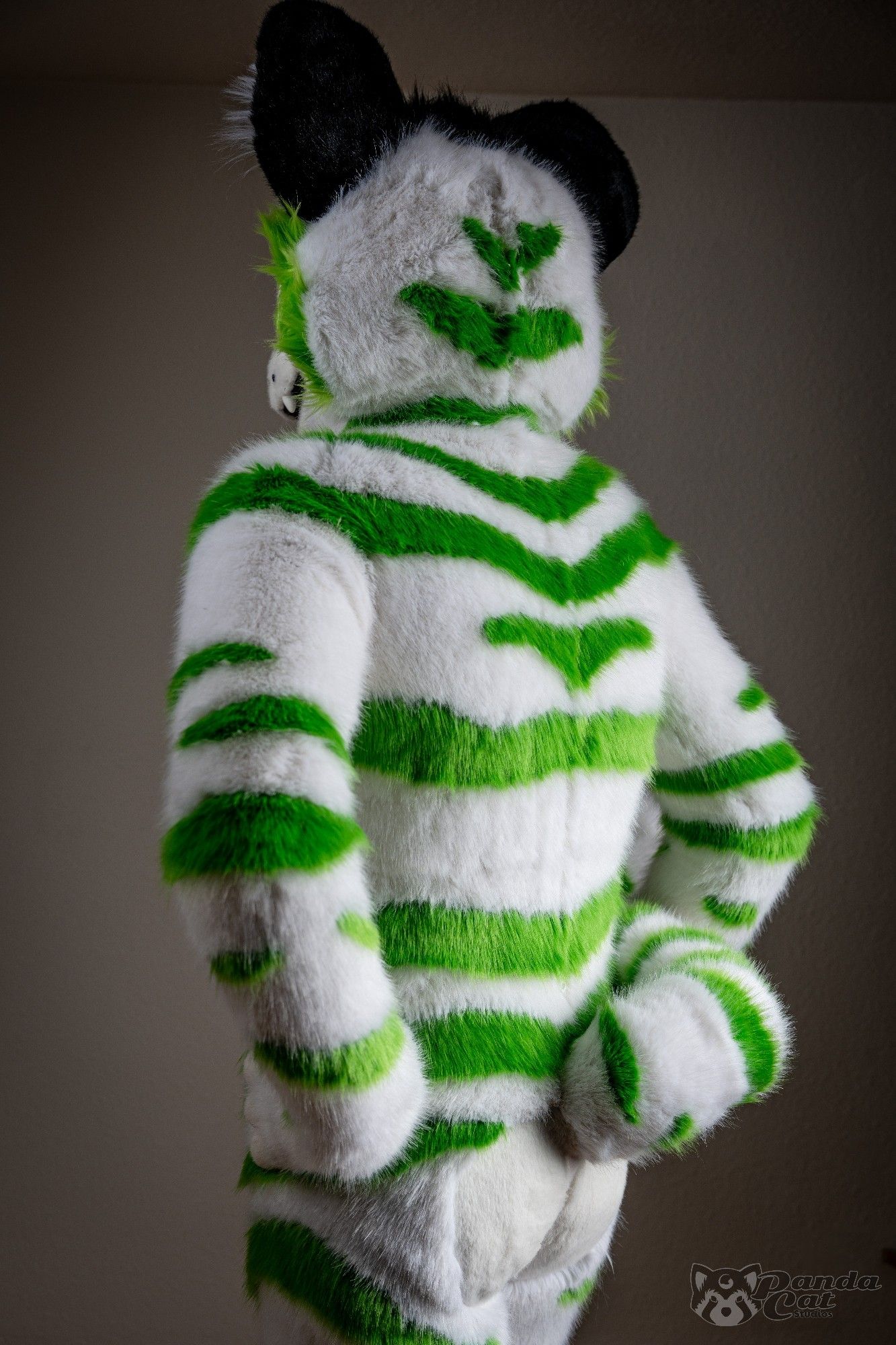 A form-fitting white tiger fursuit with detailed green stripes, viewed from slightly below the beltline. He is looking away from the camera, hands on his hips, showing off his stripes.