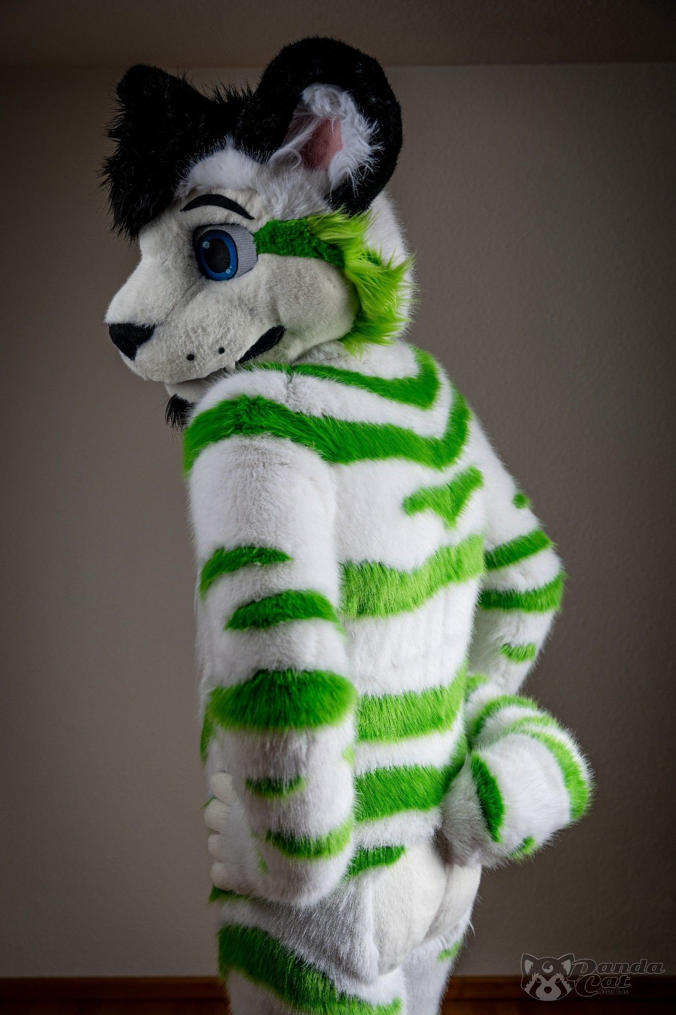 A form-fitting white tiger fursuit with detailed green stripes, viewed from slightly below the beltline. He is looking slightly over his shoulder so we can see his profile, hands on his hips.