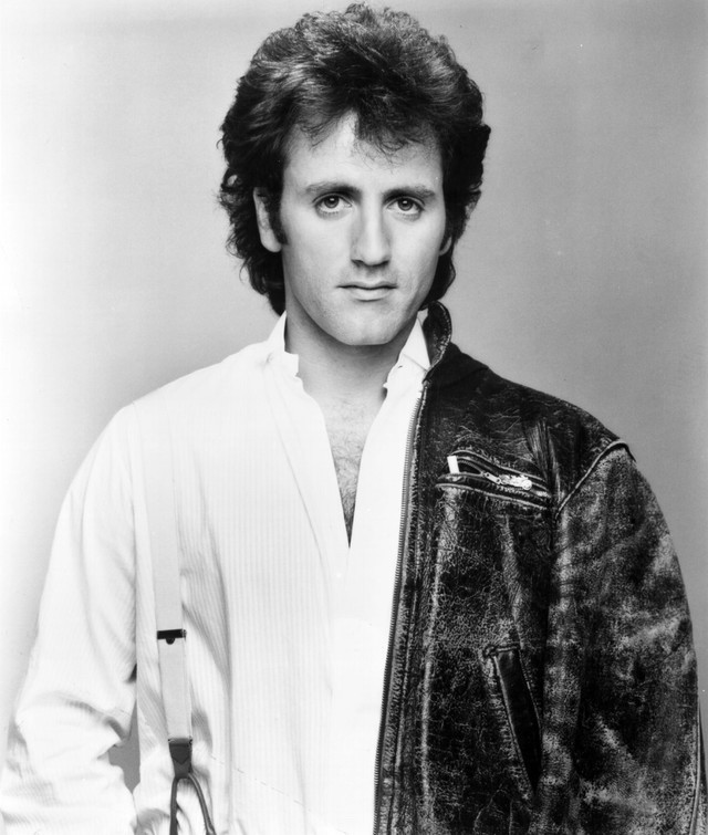 Publicity B&W shot of musician Frank Stallone c. Early to mid nineties (liberally used as a punchline by then Weekend Update host Norm MacDonald). Stallone has an early nineties cheese rocker haircut going, big but not long. He has leather jacket falling off the left shoulder and suspenders in the right one over a white button down shirt. More information on Wikipedia (Frank Stallone, Sylvester Stallone, Norm MacDonald, Rocky III, Survivor (band), “Eye of the Tiger” (song), etc.)