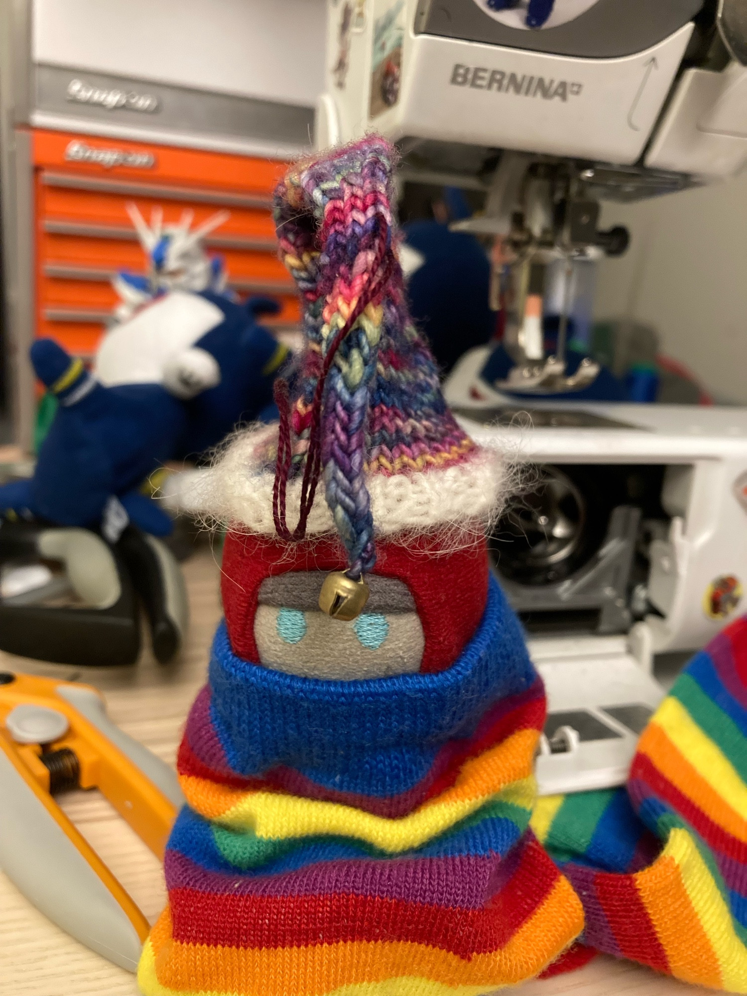 Custom miniature Swoop plushie stuffed into a rainbow sock wearing a knitted hat