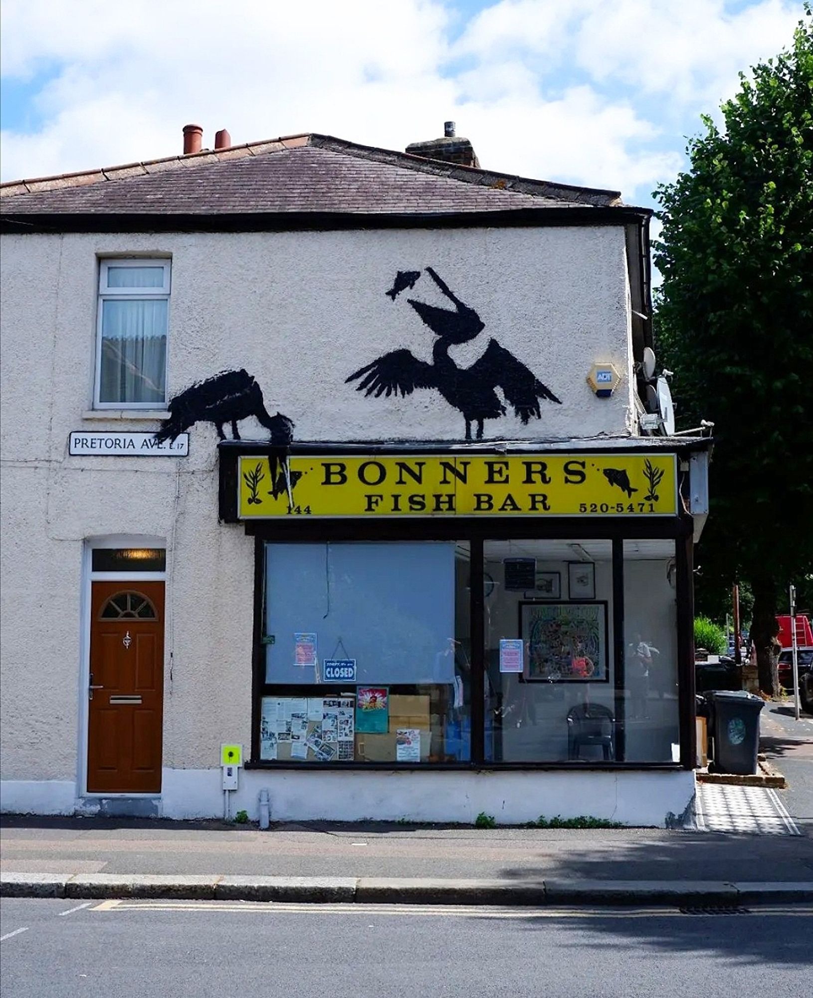 Streetartwall. A new Banksy featuring two black herons has appeared on the façade of a single-storey building with a fish takeaway. The two large birds were sprayed around the yellow store sign "Bonners Fishbar". One stands on the sign with its beak open and devours a fish, the other stands next to it and grabs another fish directly on the sign. (The photo shows the store below, a brown door and a street sign)
Note: The photo is not by Banksy this time, but by a female vlogger. She was quicker. A context has not yet been published. 09.08.2024. Five days, five Banksys...