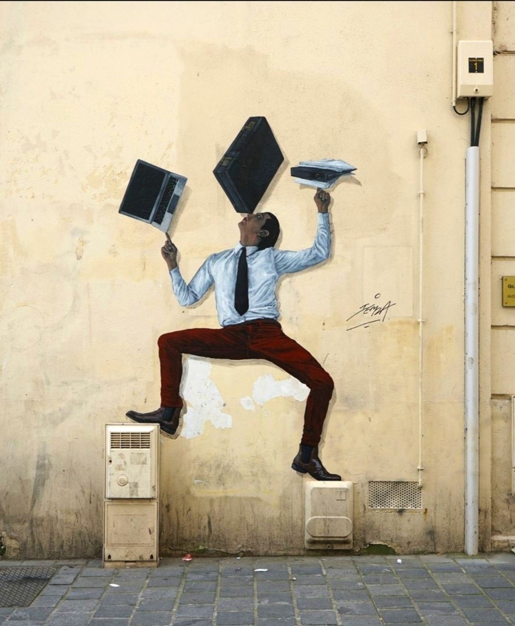 Streetartwall. A self-painted mural of a man juggling has been stuck on a yellow wall. The dark-haired man with a white shirt, black tie and red trousers is standing with his legs apart on two distribution boxes of different sizes. With his arms outstretched, he juggles a tablet on one finger, folders and papers on the other hand and a black briefcase on the tip of his nose.
Info: The artist Charles Leval, alias Levalet, is now exhibited in museums. He stands out from the usual forms of street art, as his scenes, lovingly drawn with ink on paper, show figures in their (often tragic-comic) everyday lives. They seem like repressed, unconscious feelings and experiences. They often fill long walls and are even told as serial stories.