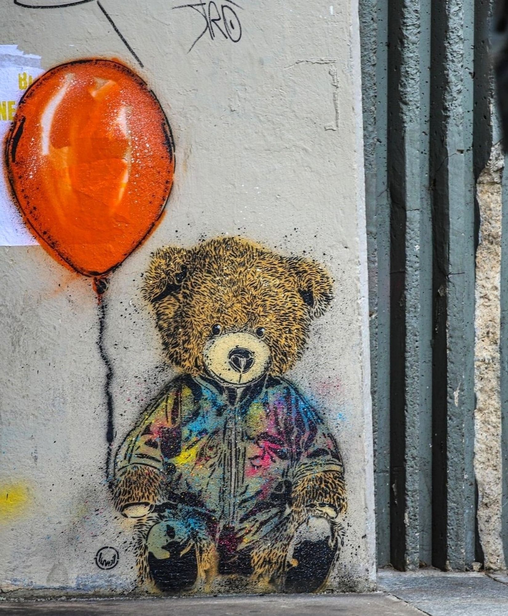 Streetartwall. A small mural depicting a brown teddy bear was sprayed with stencils on a white exterior wall of the Centre Pompidou in Paris. Wearing a jacket decorated with splashes of paint, he is sitting on the floor and holding a flying red balloon with his paw. A really cute teddy bear in a special place.
Info: The Centre Pompidou is a modern architectural marvel, recognizable by its escalators and giant coloured tubes. It houses the National Museum of Modern Art.