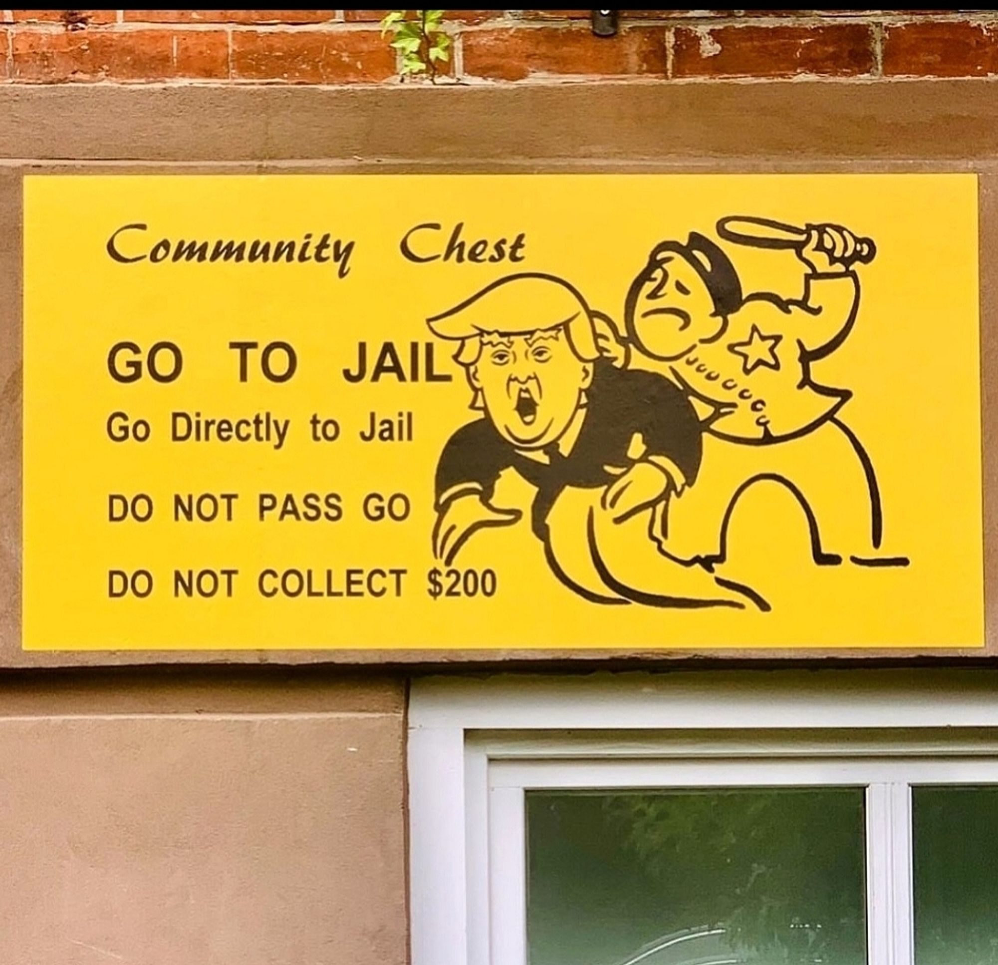 Streetartwall. A yellow poster with black text has been stuck to a brown wall with a window. It looks like a playing field/card from an old american Monopoly game. It is the prison field. A cartoon sheriff figure with a baton grabs a horrified Donald Trump by the collar. Next to it is the following text, which is based on the original: 
Community Chest, GO TO JAIL, Go straight to jail, DO NOT GO, DO NOT COLLECT $200
Info: WestvillageFamous is an anonymous designer who keeps putting up signs with mostly political and satirical messages on the wall of his house in New York.